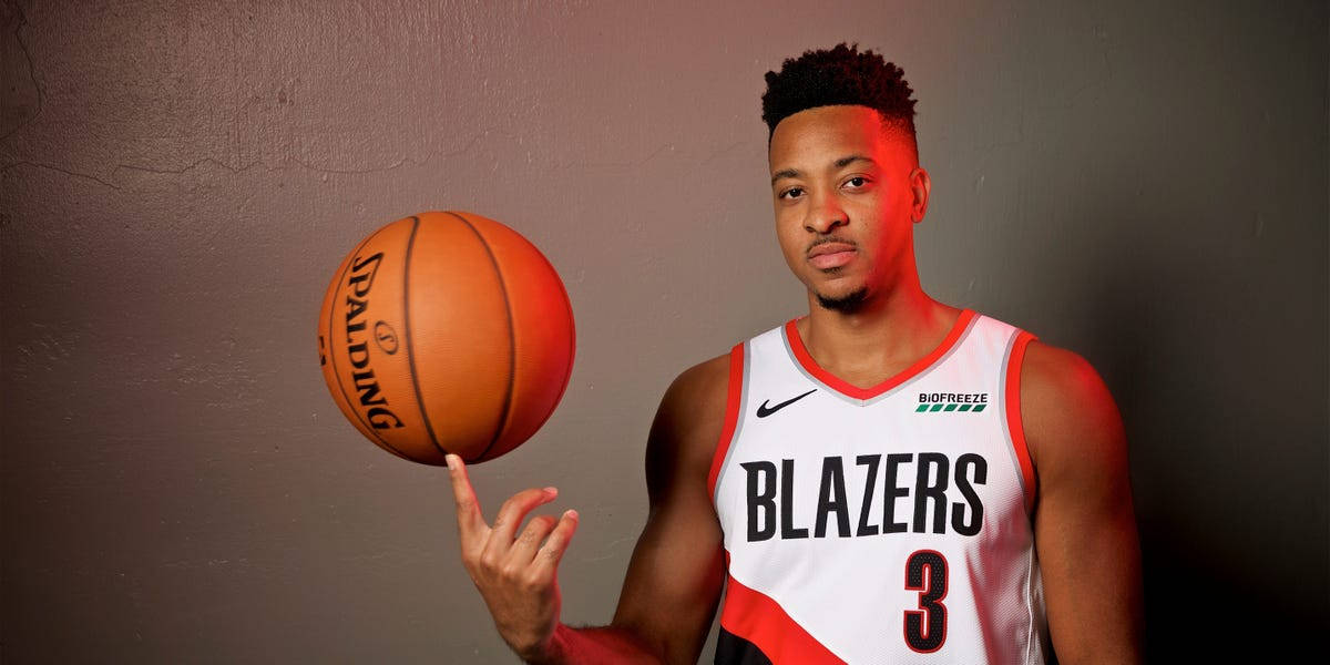 CJ麥考倫籃球肖像照 壁紙 — 一名身穿 Blazers 球衣的籃球運動員在柔和的灰色牆壁前，用指尖平衡一個橙色的 Spalding 籃球。