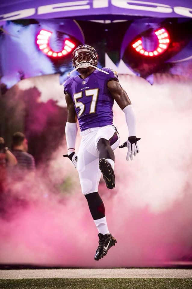 美式足球線衛CJ Mosley 預賽季亮相 壁紙 — 巴爾的摩烏鴉隊身穿紫色球衣57號的美式足球員在球場燈光下動態地跳過粉紅色煙霧。