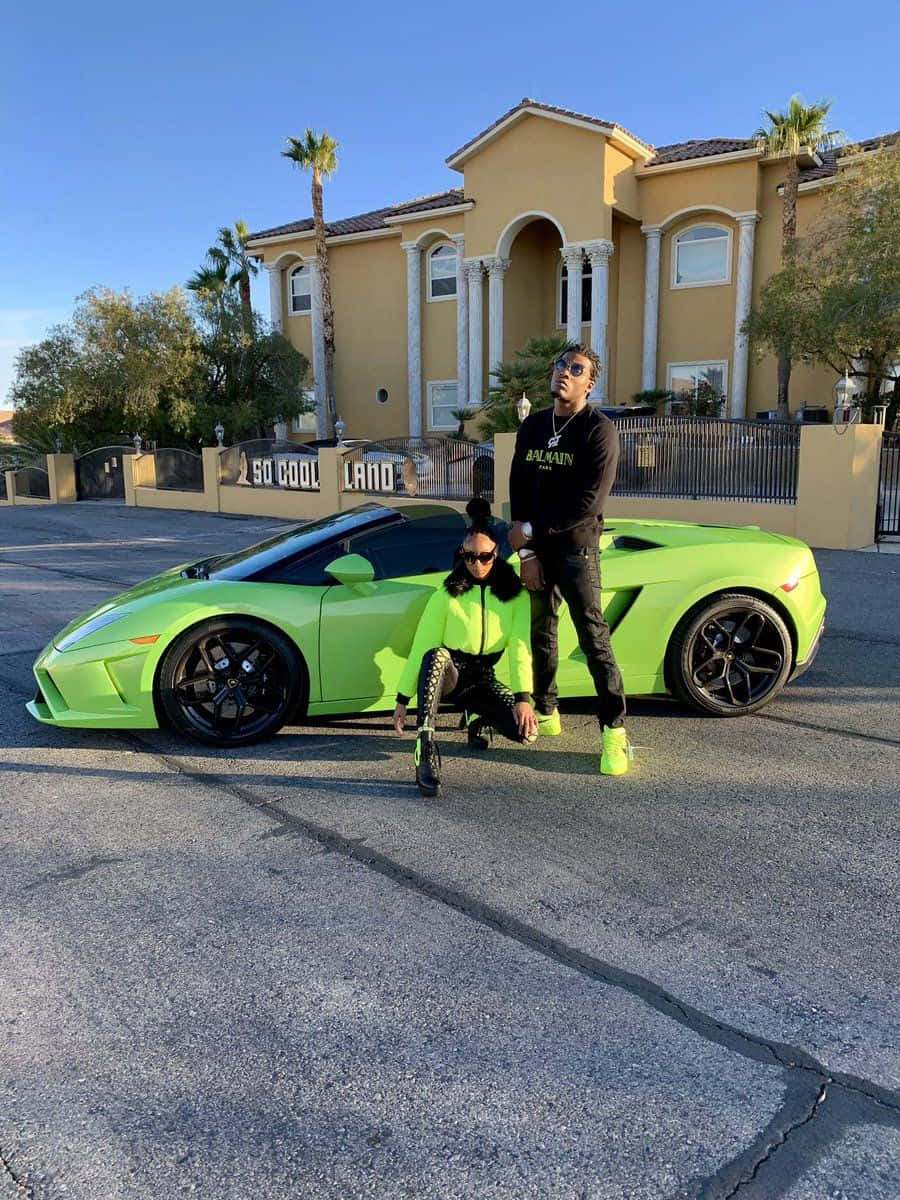 兩位穿著相配螢光服裝的人在豪宅前與一輛綠色跑車合照。