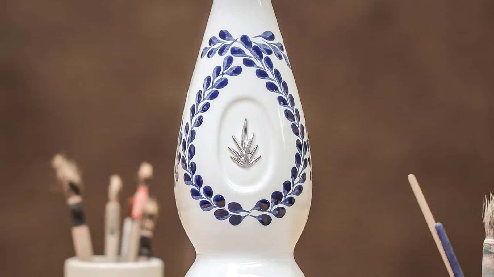 白色陶瓷花瓶，帶有藍色葉子設計和銀色標誌，被畫筆環繞。