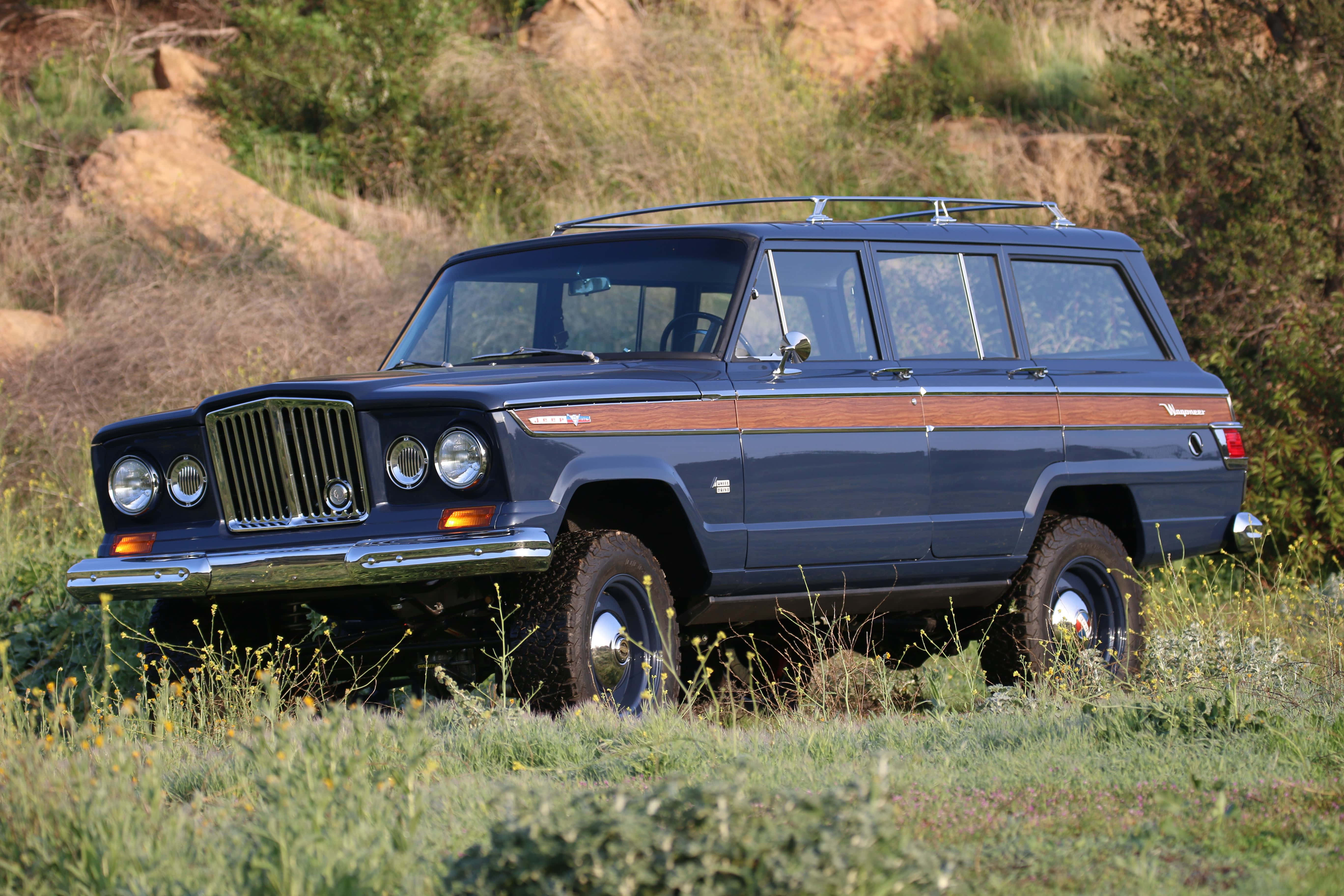 Jeep Wagoneer 桌布 壁紙 — 經典藍色Jeep Wagoneer配木飾邊，停泊在草地地形上，處於明亮日光下。