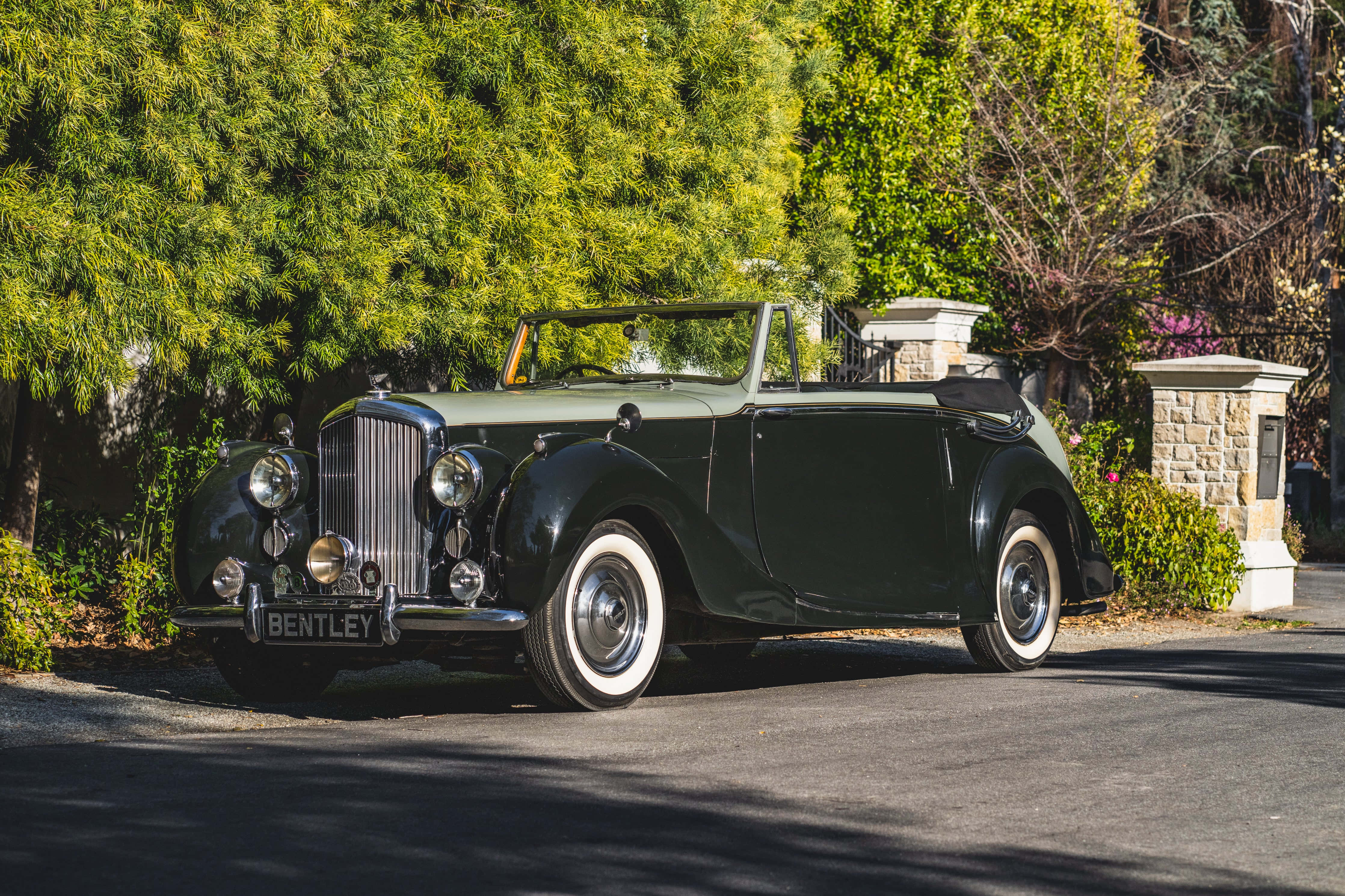Bentley Mark Vi 桌布 壁紙 — 一輛經典綠色賓利開篷車停泊在陽光普照的車道上，旁邊是茂密的綠色樹籬和石柱。