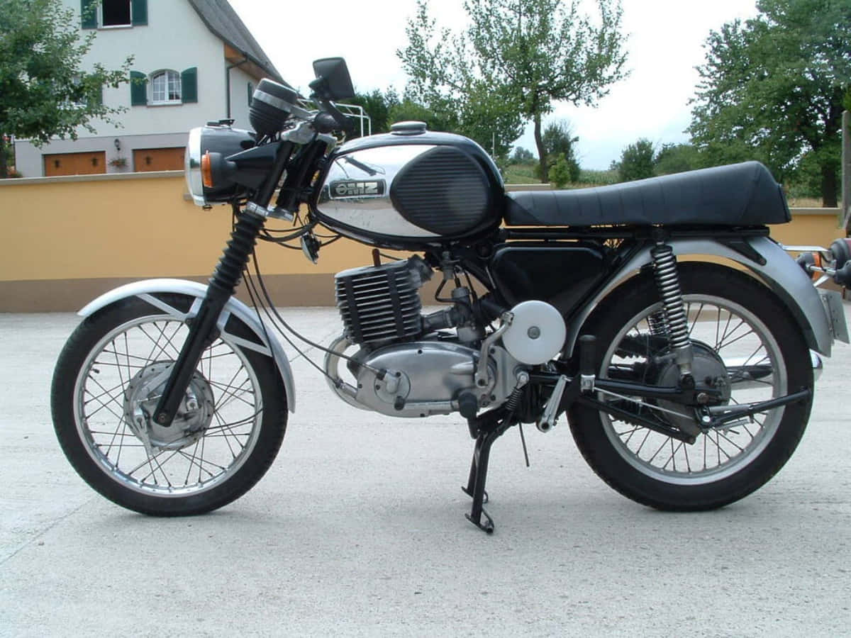Mz Motorcycle 桌布 壁紙 — 一輛經典銀黑色Oriz電單車停泊在混凝土車道上，背景有房屋和樹木。