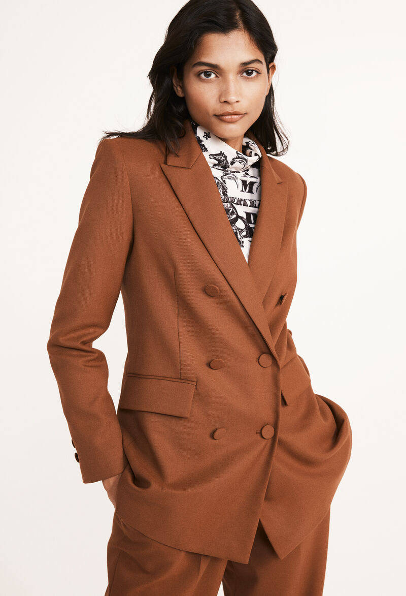 Claudie Pierlot棕色正式西裝外套：優雅的化身 壁紙 — 一位穿著訂製鏽色雙排扣西裝的女性自信地站在純白色背景前。