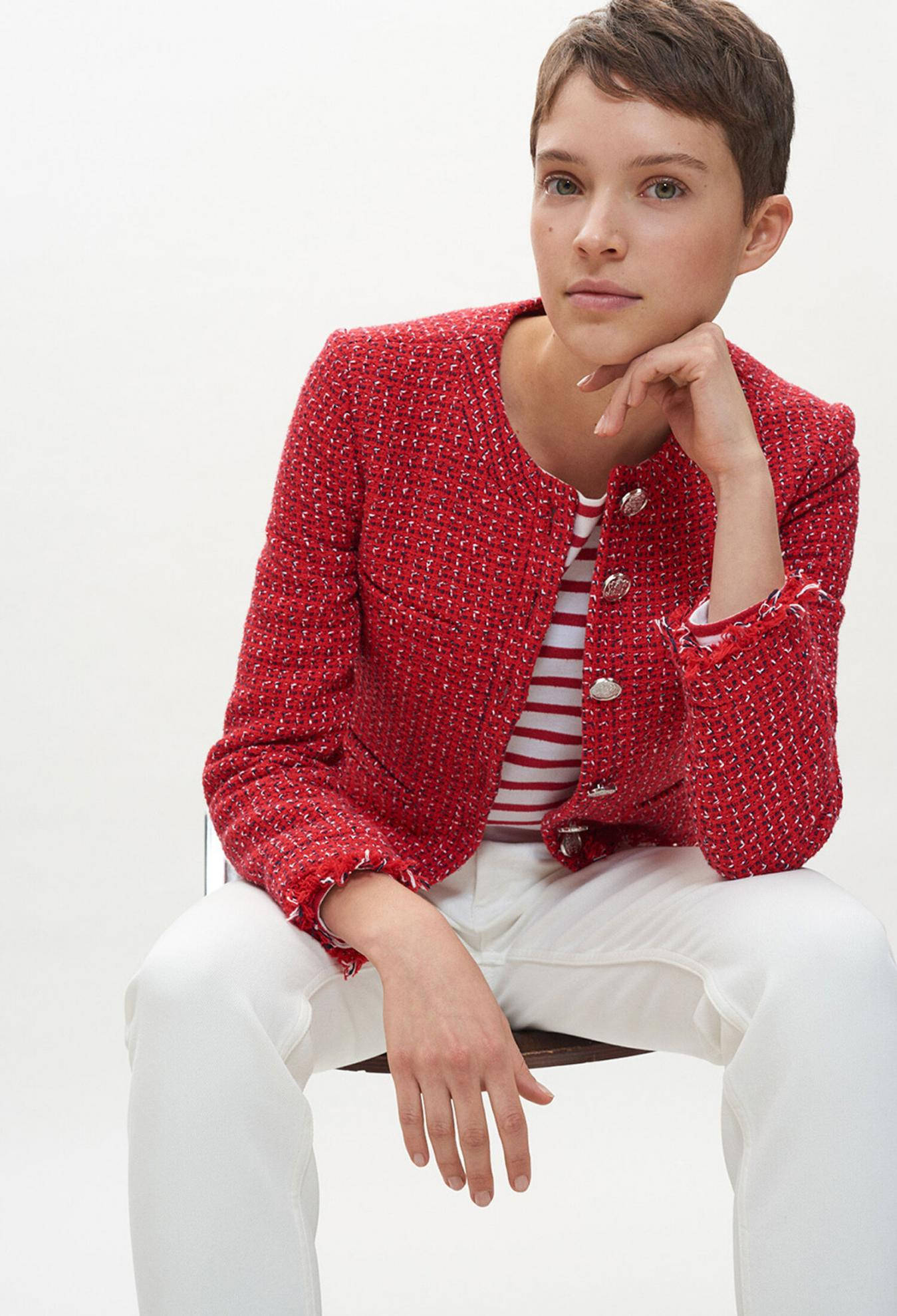 Claudie Pierlot時尚前衛紅色粗花呢西裝外套 壁紙 — 一位短髮女性身穿有紋理的紅色外套，內搭條紋襯衫，坐在純白背景前，姿態優雅。