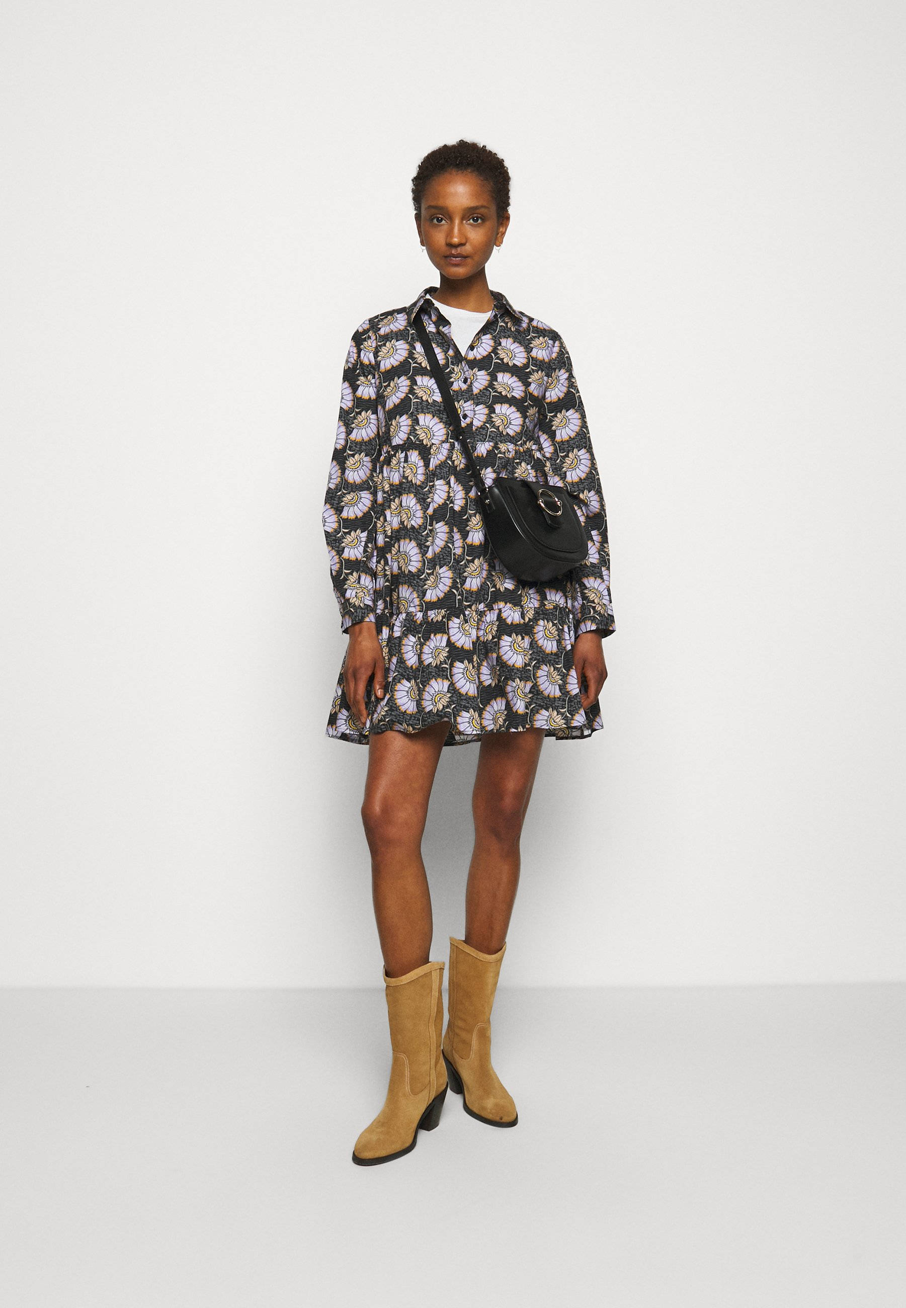 Claudie Pierlot 絢麗花卉Polo連衣裙 壁紙 — 一位女士自信地穿著花卉印花襯衫裙和棕褐色靴子，站在純白色工作室背景前。