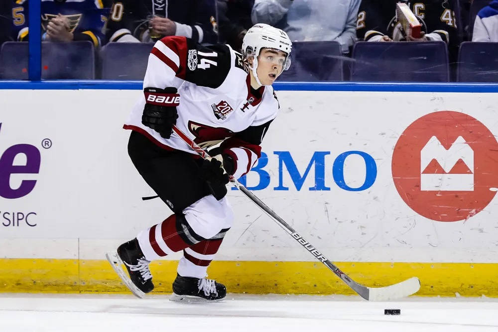 Clayton Keller 亞利桑那郊狼隊NHL首秀 壁紙 — 一名身穿白色和紅色裝備的冰球運動員在比賽中於冰上激烈滑行，球桿上帶著冰球。