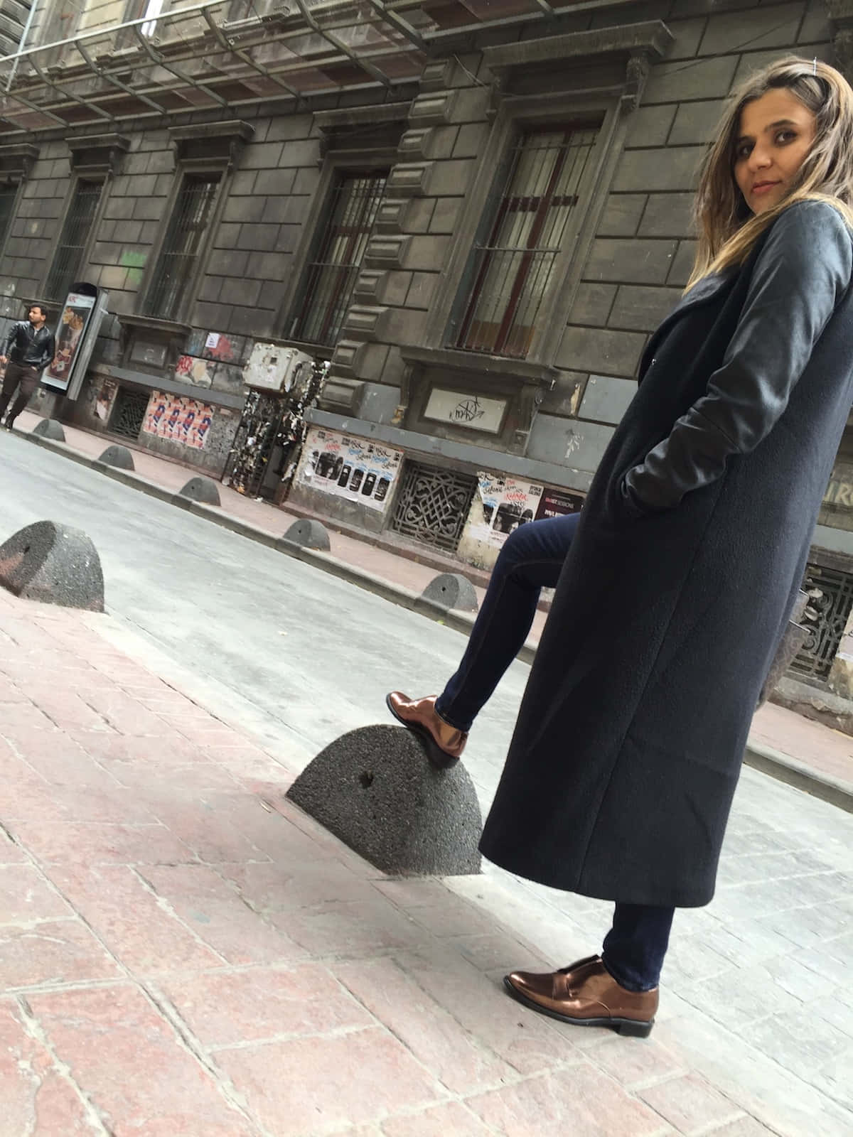 身穿深色外套的女性在城市人行道的石柱上保持平衡
