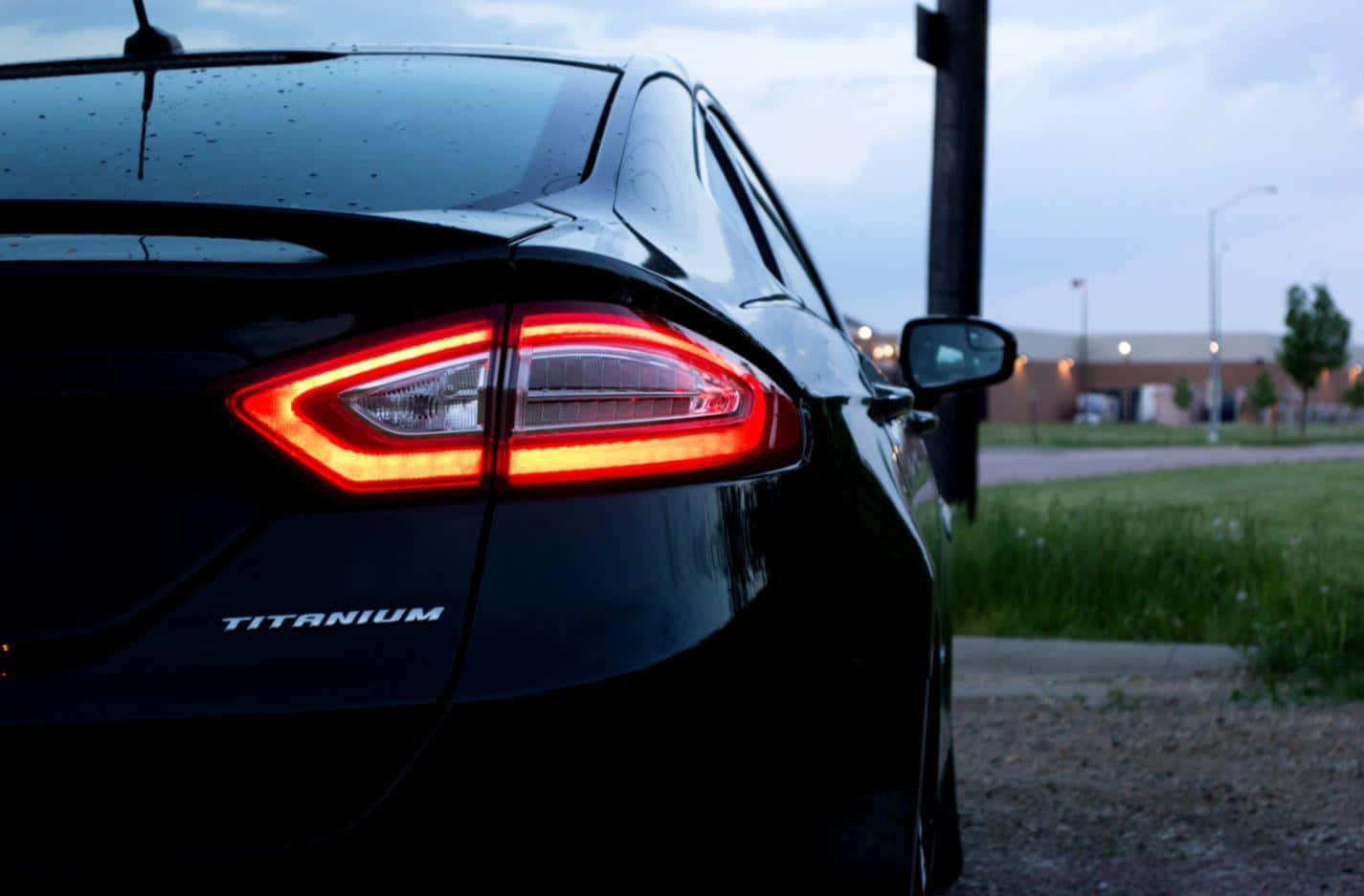 Ford Fusion 桌布 壁紙 — 近距離拍攝黑色福特 Fusion Titanium 在黃昏時發光的紅色尾燈，後窗上有雨滴。