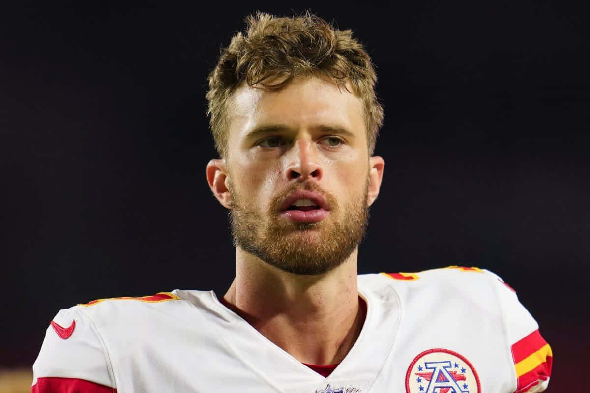 Harrison Butker 桌布 壁紙 — 特寫鏡頭，一名專注的足球運動員身穿帶有紅色和黃色點綴的白色球衣，背景為深色。
