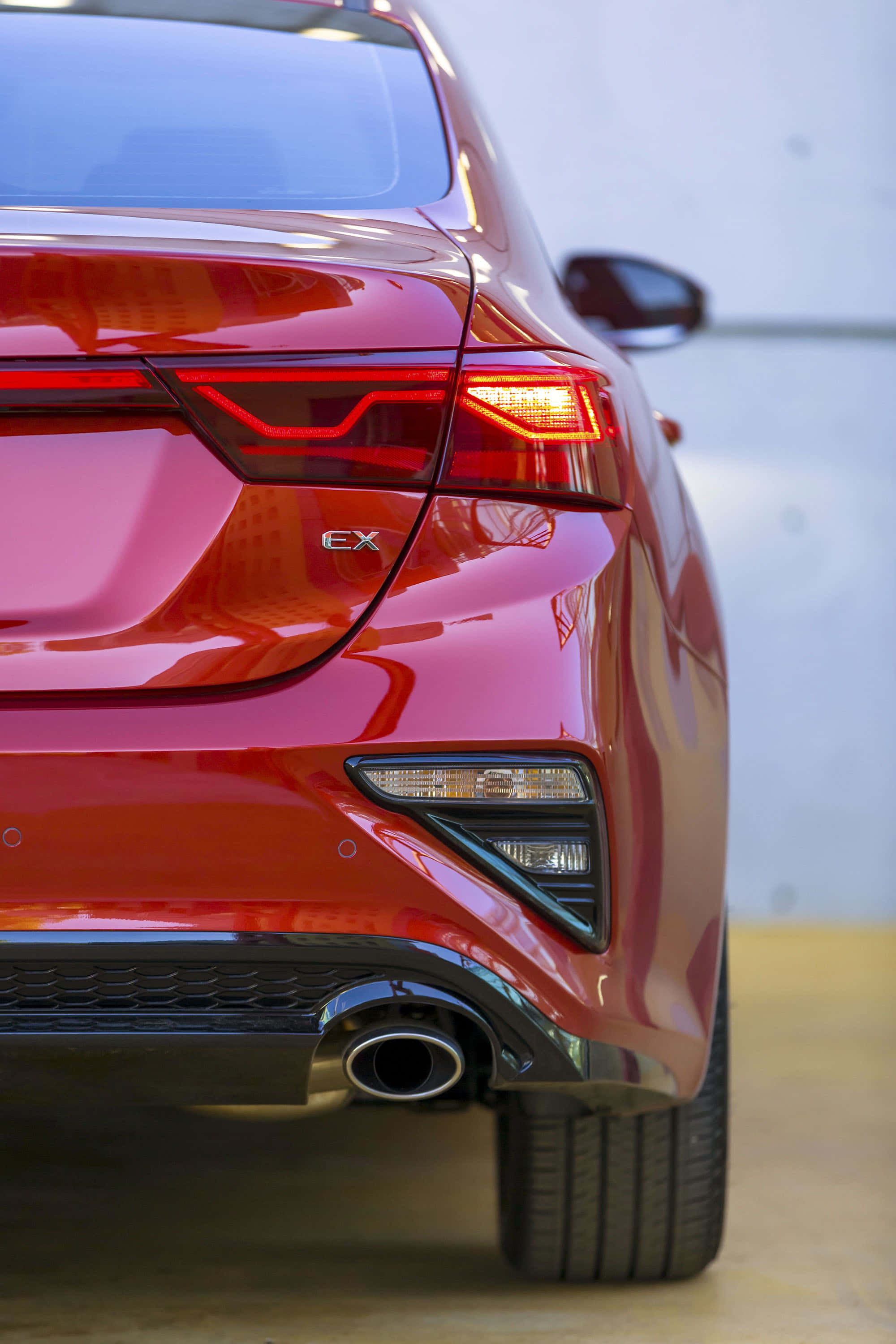 Kia Forte 桌布 壁紙 — 光面紅色汽車尾部的特寫，展示時尚的尾燈和排氣管，背景簡潔。