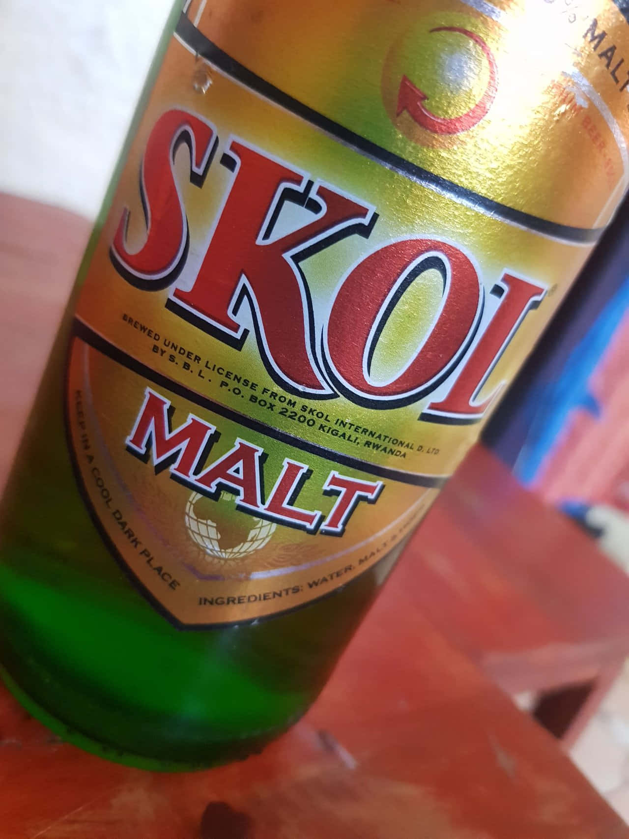  壁紙 — 綠色玻璃Skol Malt啤酒瓶的特寫，帶有金色和紅色標籤，放置在微紅的木質表面上。