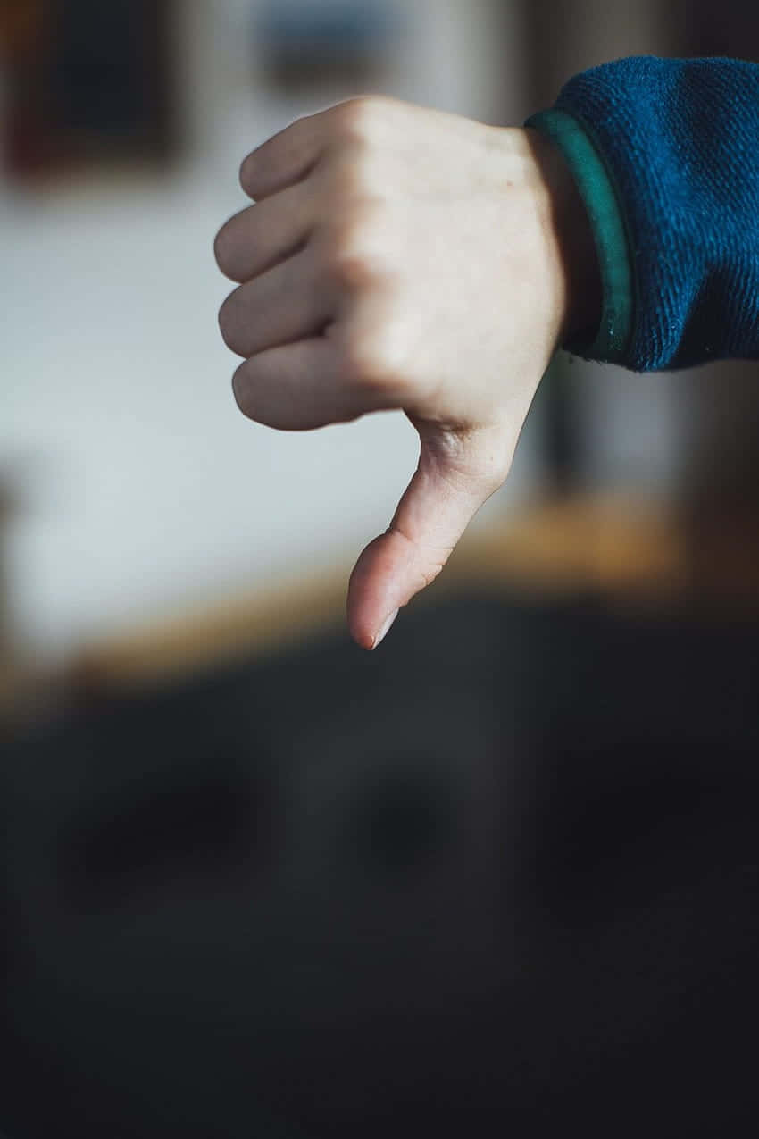  壁紙 — 一隻手在模糊的室內背景下做出拇指向下的手勢的特寫。