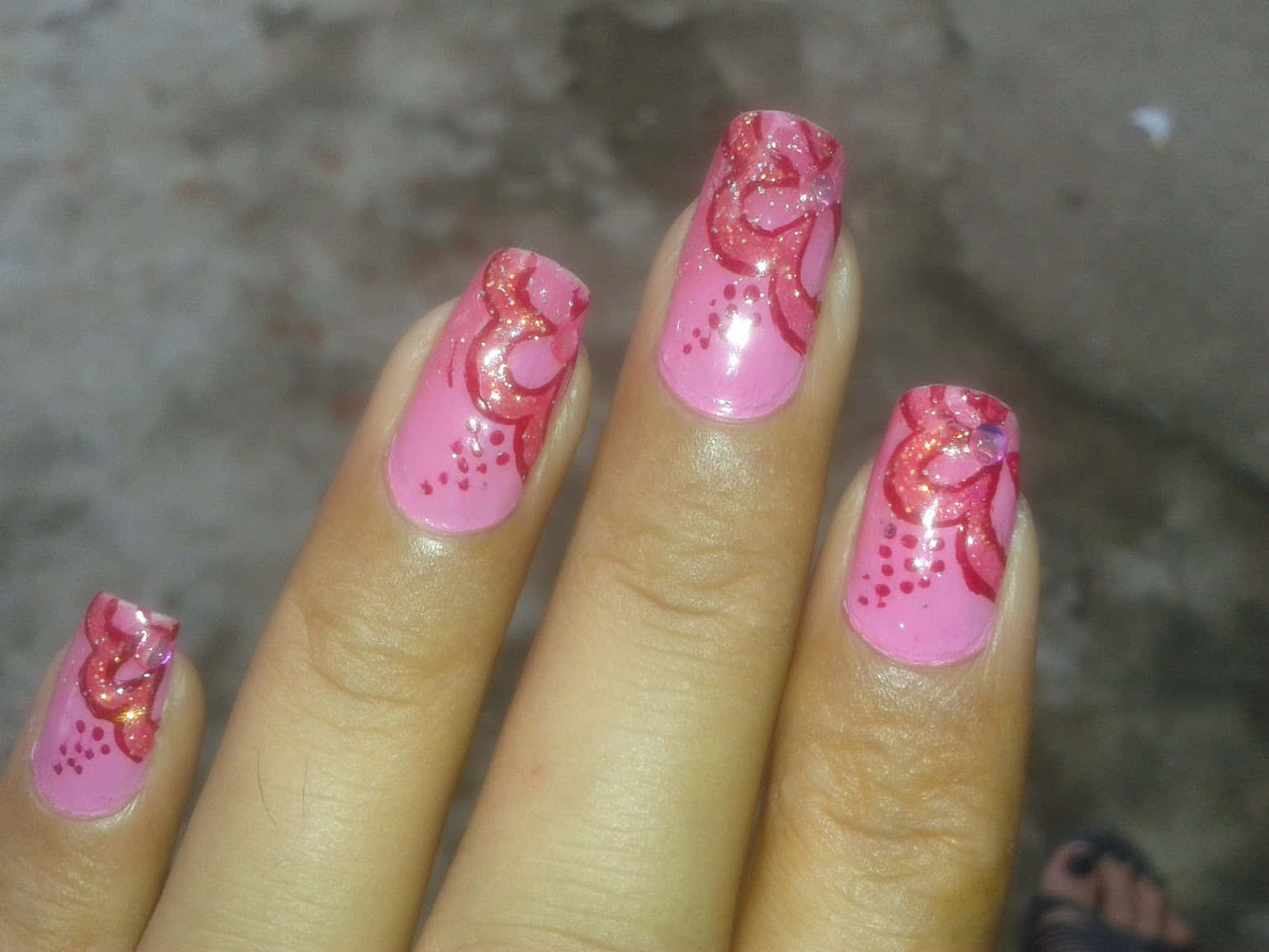 Pink Nails 桌布 壁紙 — 一隻手嘅特寫，粉紅色閃粉指甲上有紅色漩渦同圓點，背景係模糊嘅混凝土。