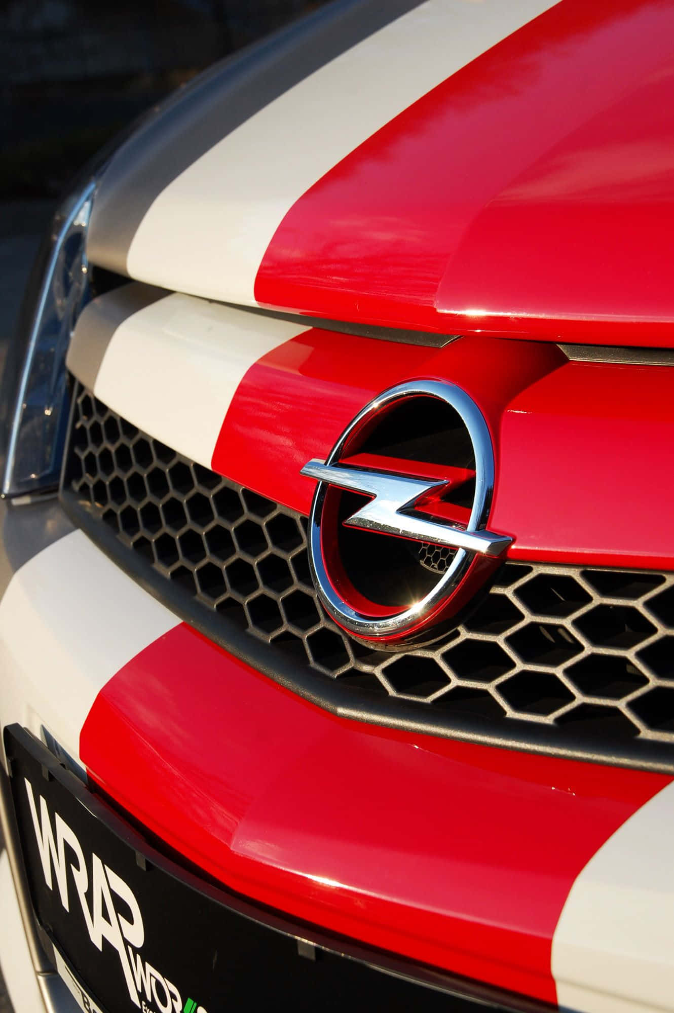 Opel Astra 桌布 壁紙 — 紅色和白色條紋歐寶汽車引擎蓋的特寫，帶有鍍鉻標誌和黑色蜂窩狀格柵。