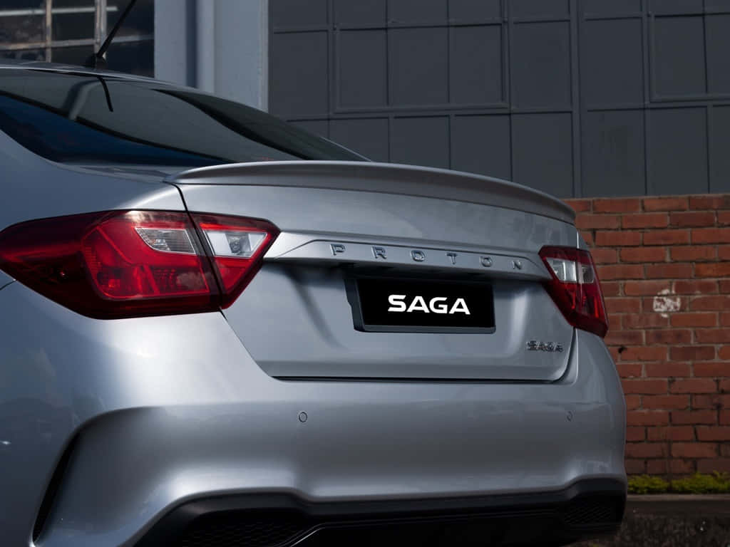  壁紙 — 銀色 Proton Saga 汽車尾部特寫，展示其尾燈和徽章，背景為磚牆和灰色建築物。
