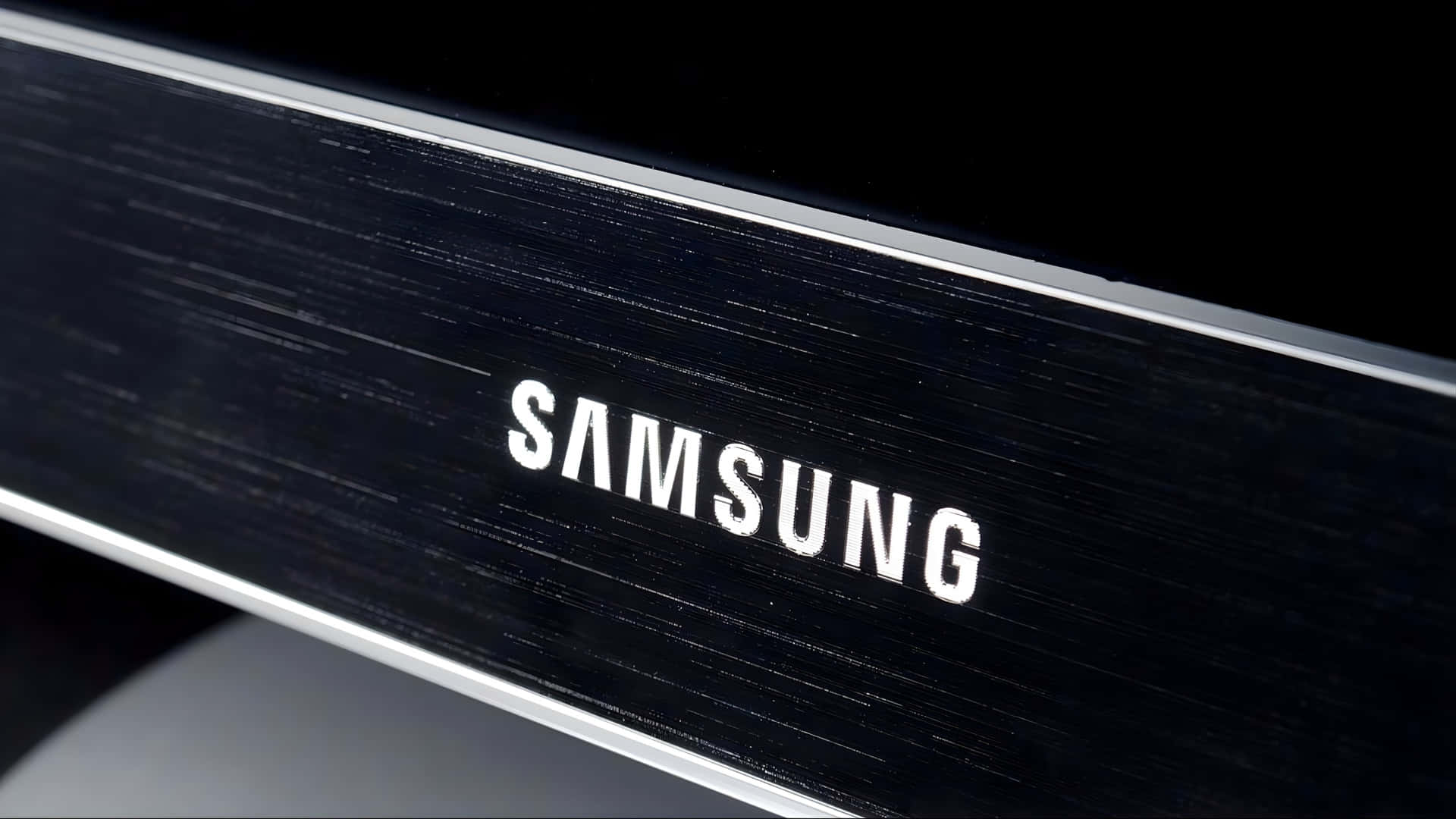  壁紙 — 特寫一個時尚的黑色Samsung標誌，帶有拉絲金屬質感和銀色飾邊，背景為深色。
