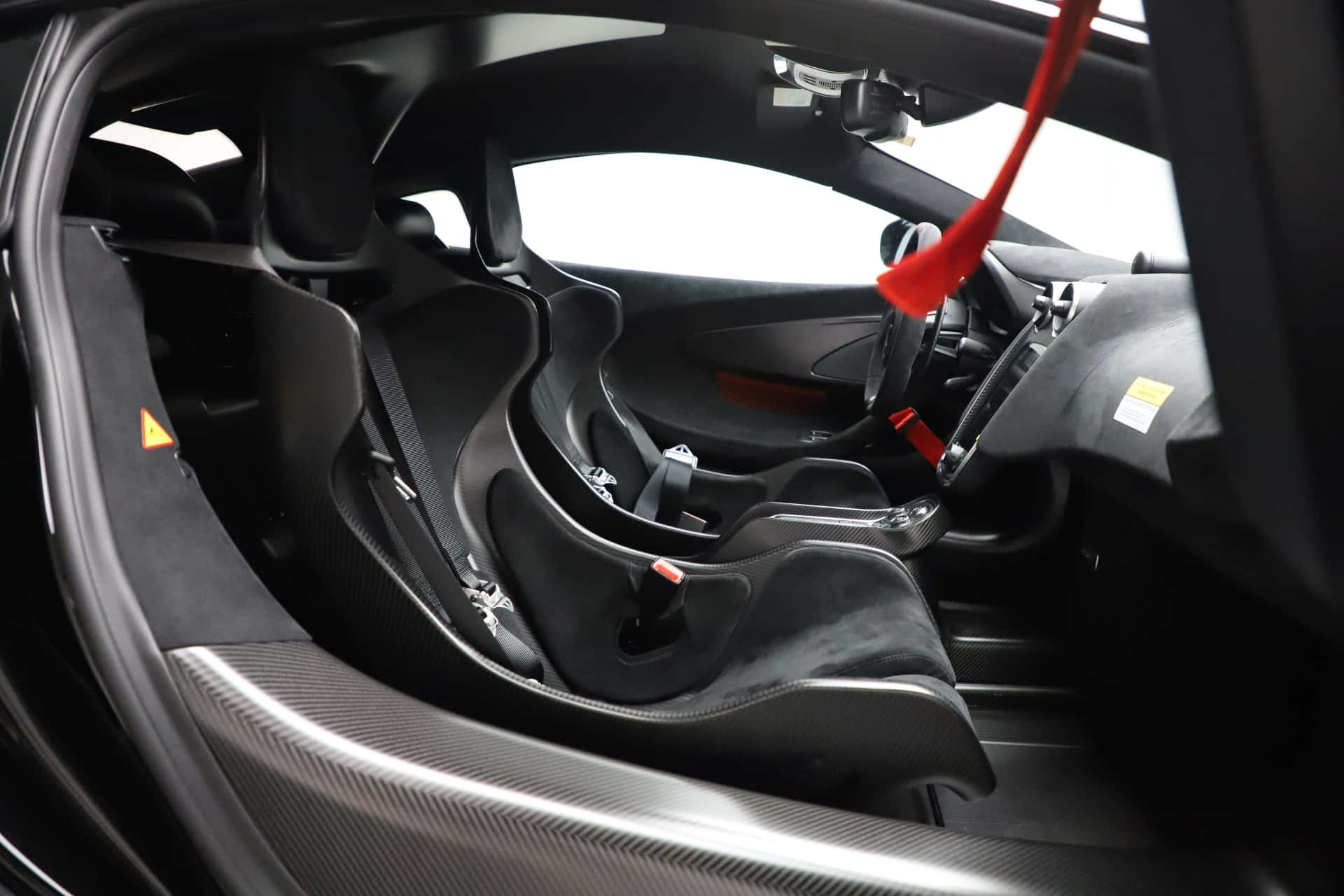 Mclaren 620r 桌布 壁紙 — 黑色跑車內飾特寫，採用碳纖維飾邊和紅色安全帶。
