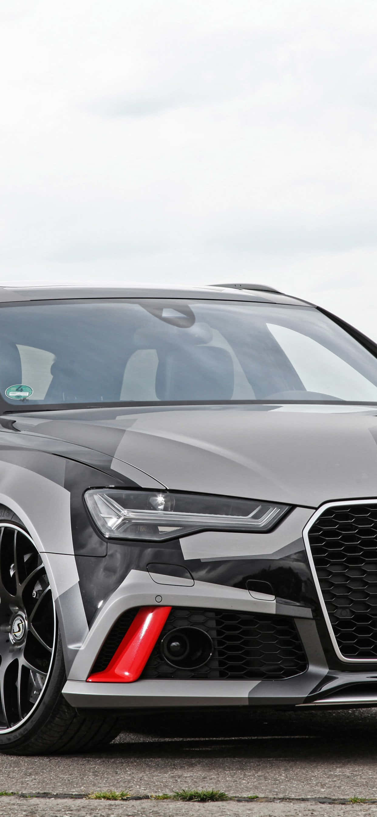 Audi Rs6 桌布 壁紙 — 灰色奧迪RS6 Avant的緊湊特寫，帶有醒目的紅色點綴和黑色輪圈，背景為多雲天空。