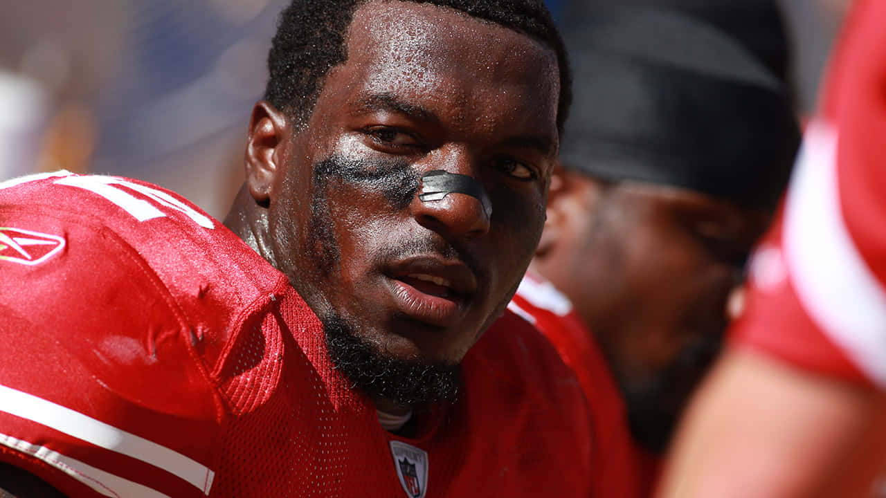 壁紙 — 近距離拍攝一名汗流浹背的足球員，身穿紅色球衣，帶黑色眼妝，在陽光普照的比賽中專注凝視。