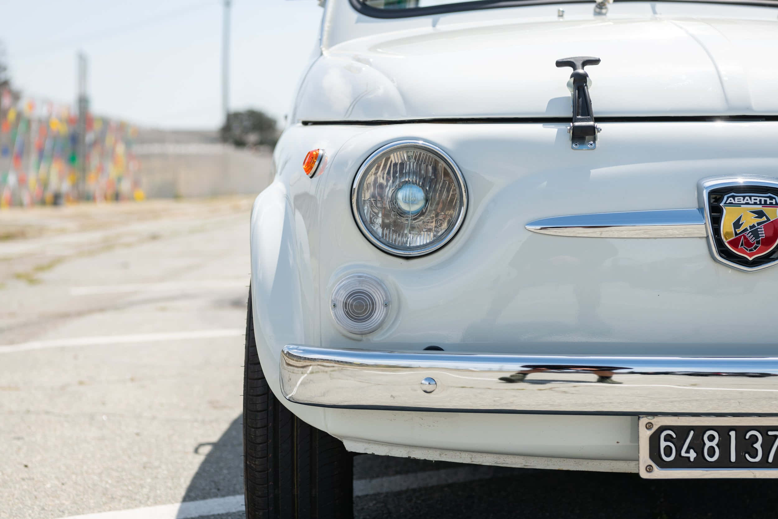 Fiat 500 桌布 壁紙 — 一輛復古白色 Fiat 500 Abarth 的特寫，帶有鍍鉻裝飾和圓形頭燈，停放在陽光普照的瀝青停車場上。