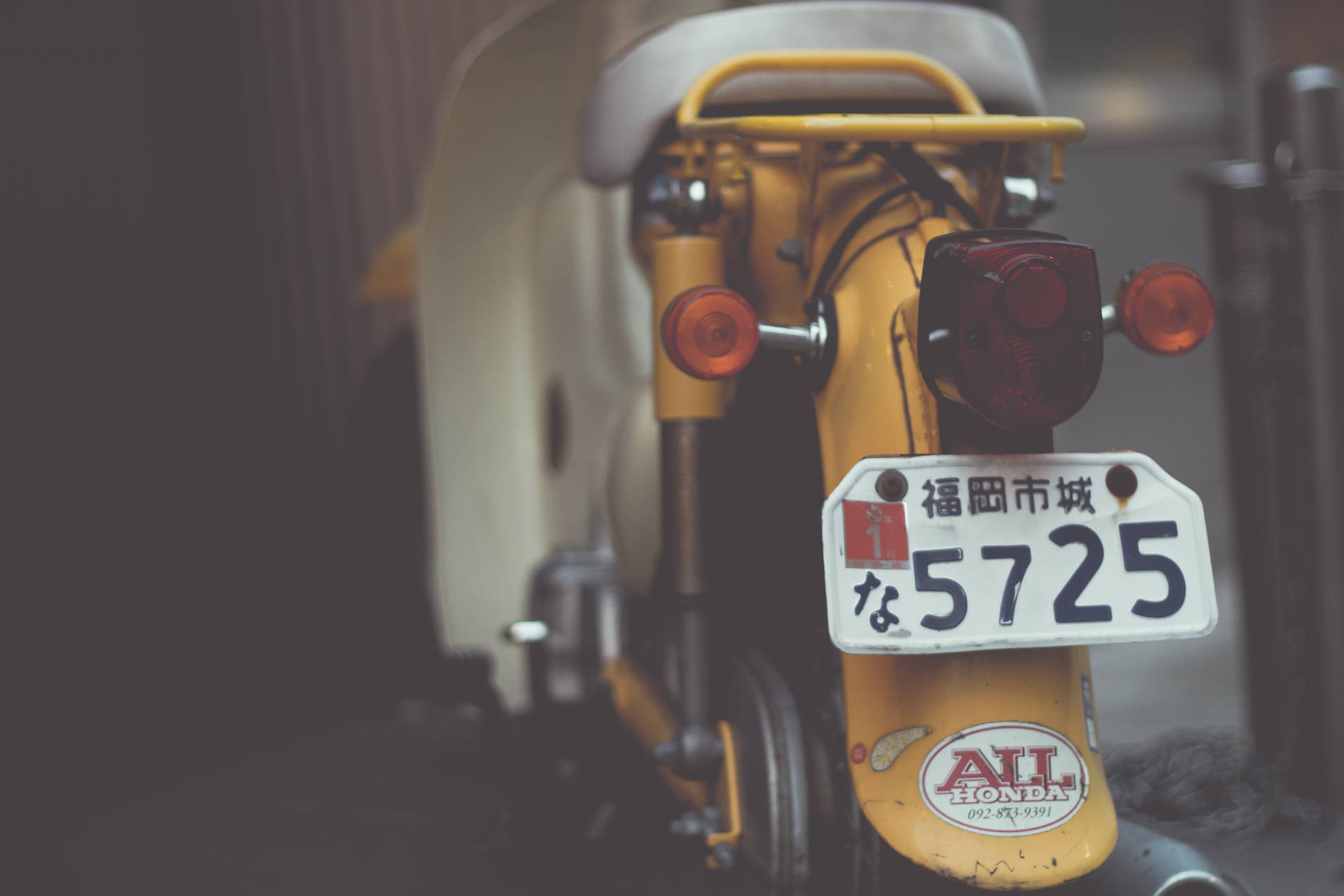 白黃色踏板摩托車 壁紙 — 復古黃色電單車後部特寫，帶有日本車牌和紅色尾燈。