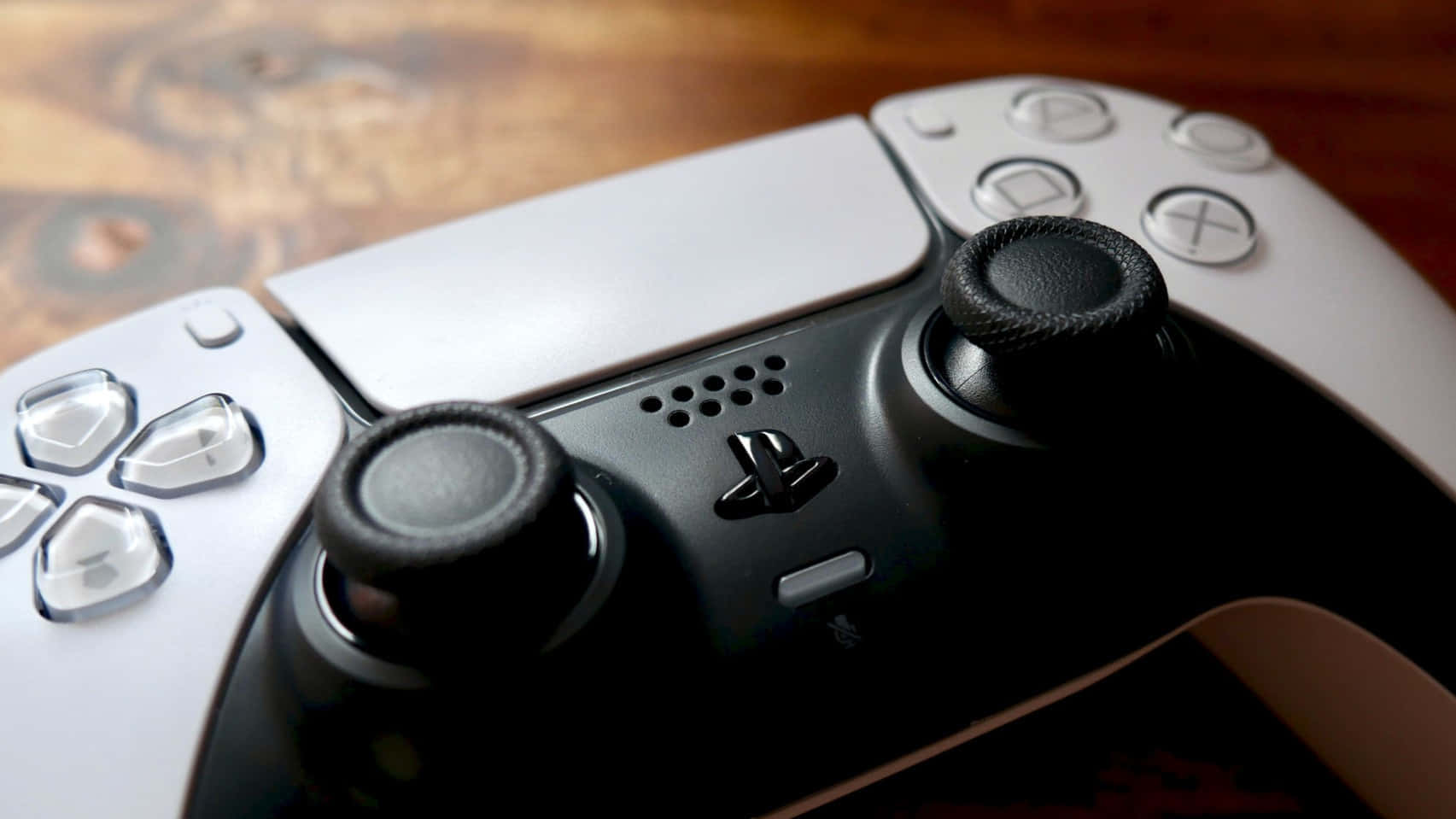  壁紙 — 白色和黑色PlayStation 5手掣的特寫，放置在木質表面上，帶有溫暖的燈光。
