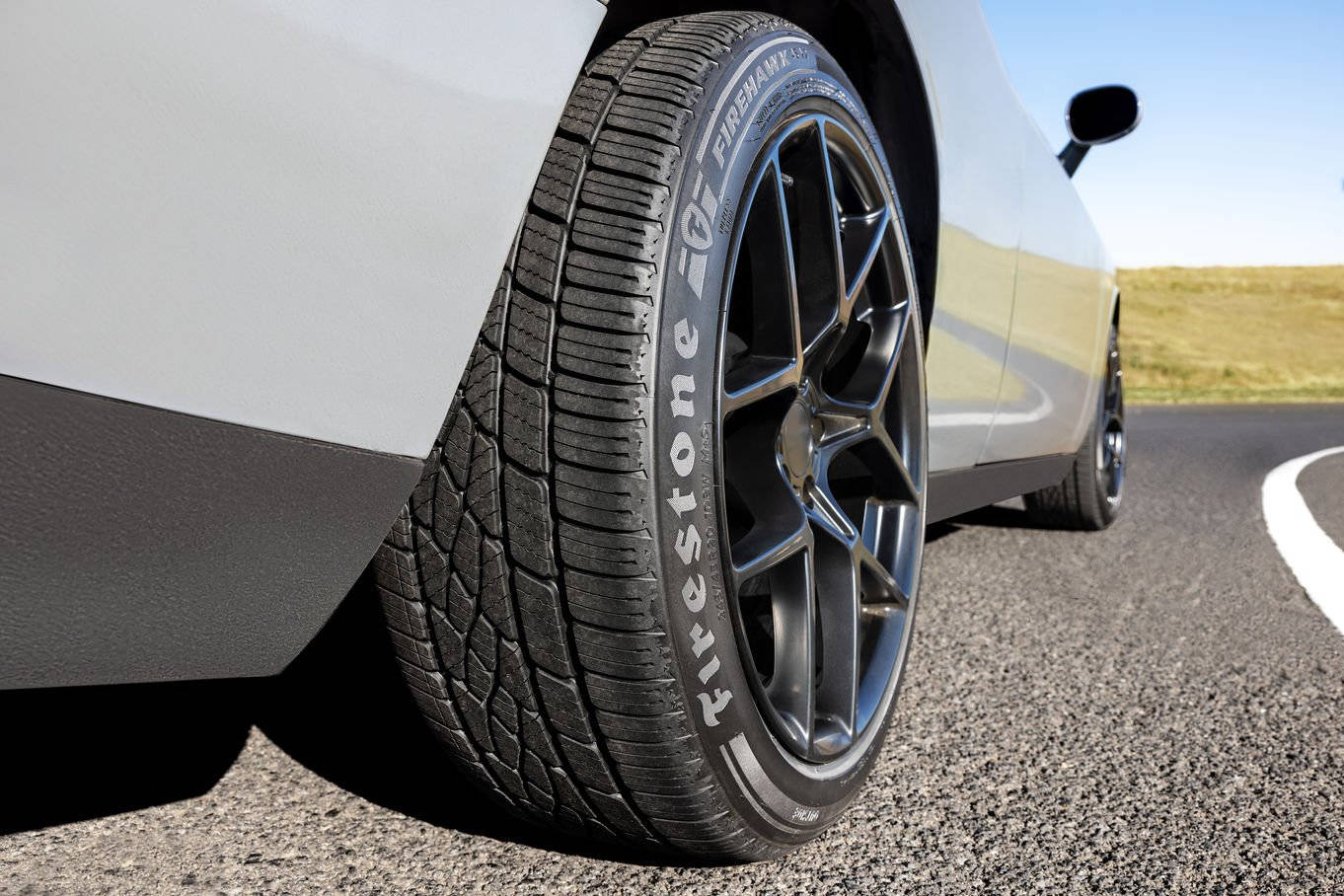 Firestone 輪胎安裝於汽車 壁紙 — 白色汽車輪胎和合金輪轂在蜿蜒的瀝青路上、明亮日光下的特寫。