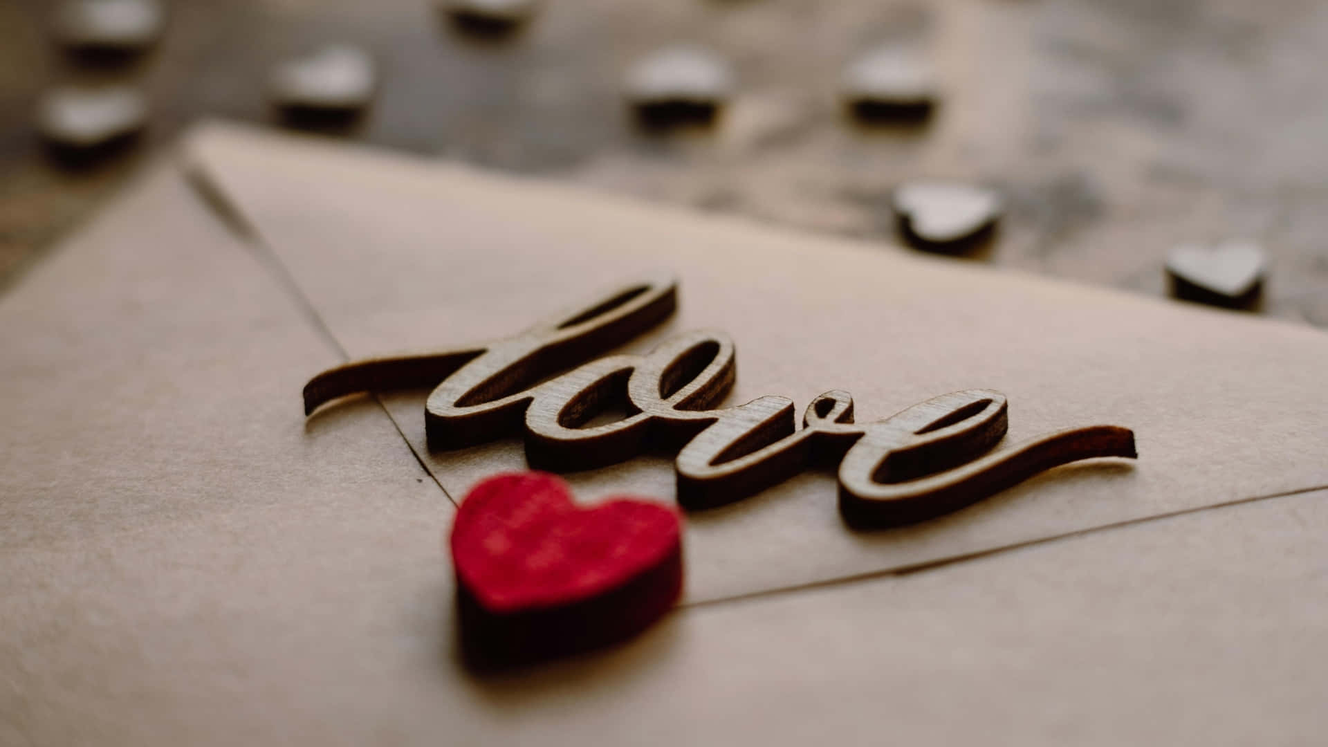  壁紙 — 一個木製嘅「love」標誌同紅色心形喺啡色信封上嘅特寫，背景有模糊嘅心形鈕扣。