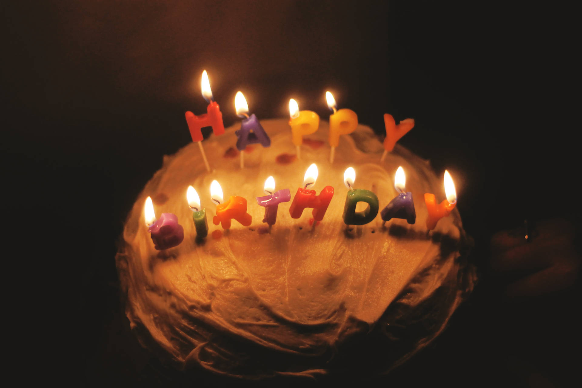 一個生日蛋糕，在黑暗環境中點燃蠟燭拼出 happy birthday 字樣。