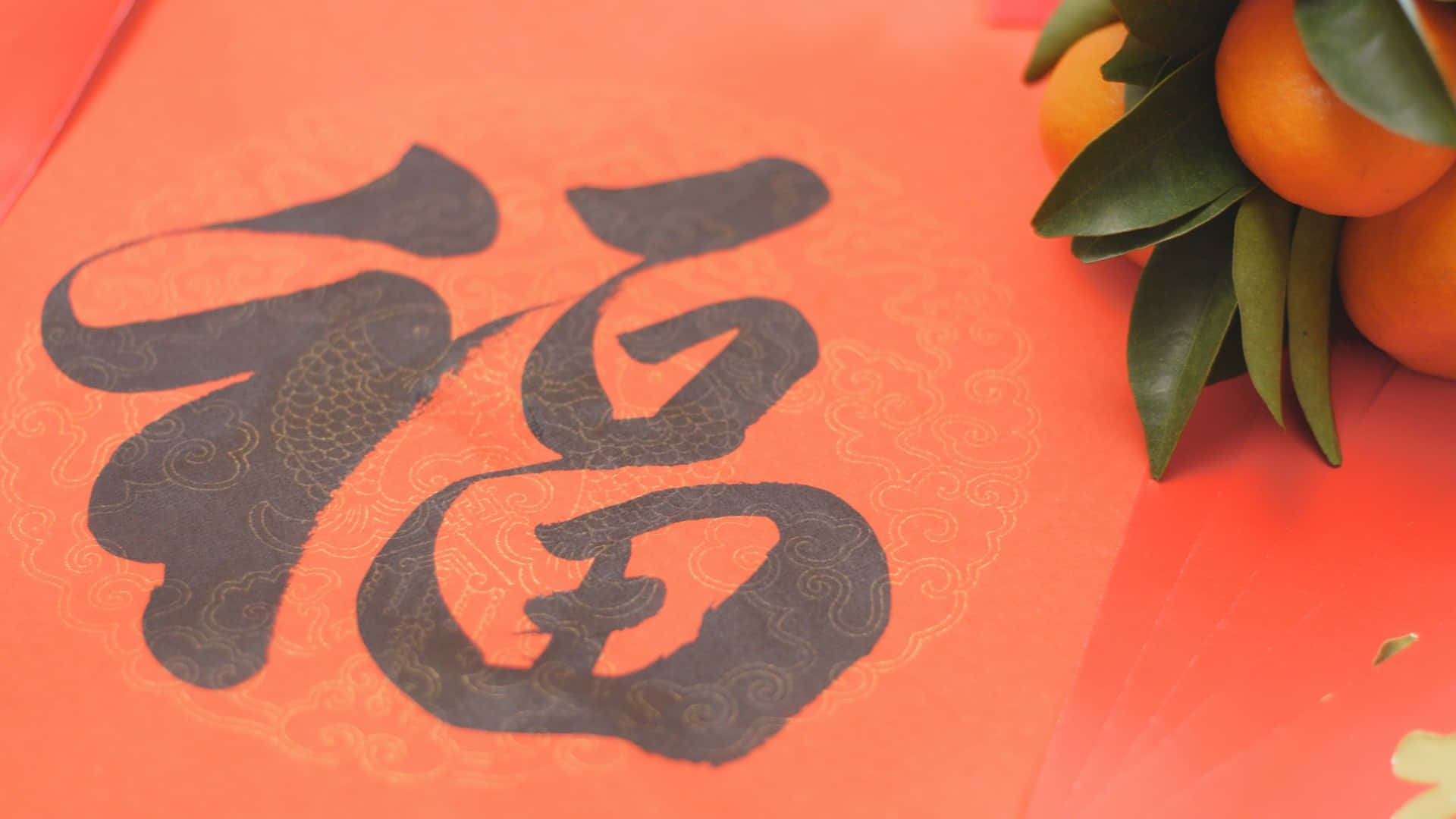  壁紙 — 一個大膽的黑色漢字「福」的特寫，位於鮮豔的橙色紙上，旁邊有新鮮的柑橘和綠葉。