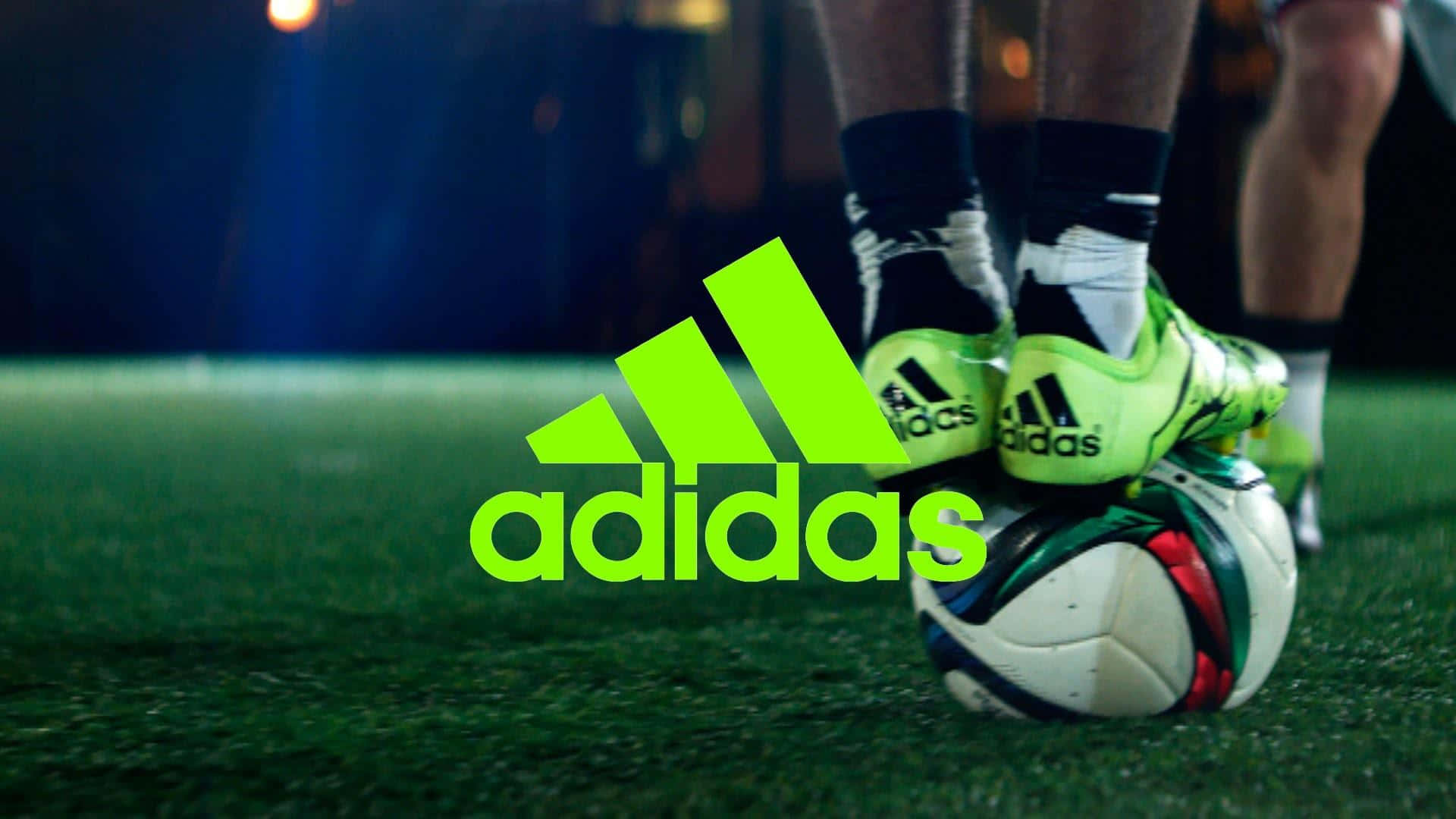 足球美學：Adidas標誌 壁紙 — 球場燈光下，人造草地上足球上的螢光綠色adidas球鞋特寫。