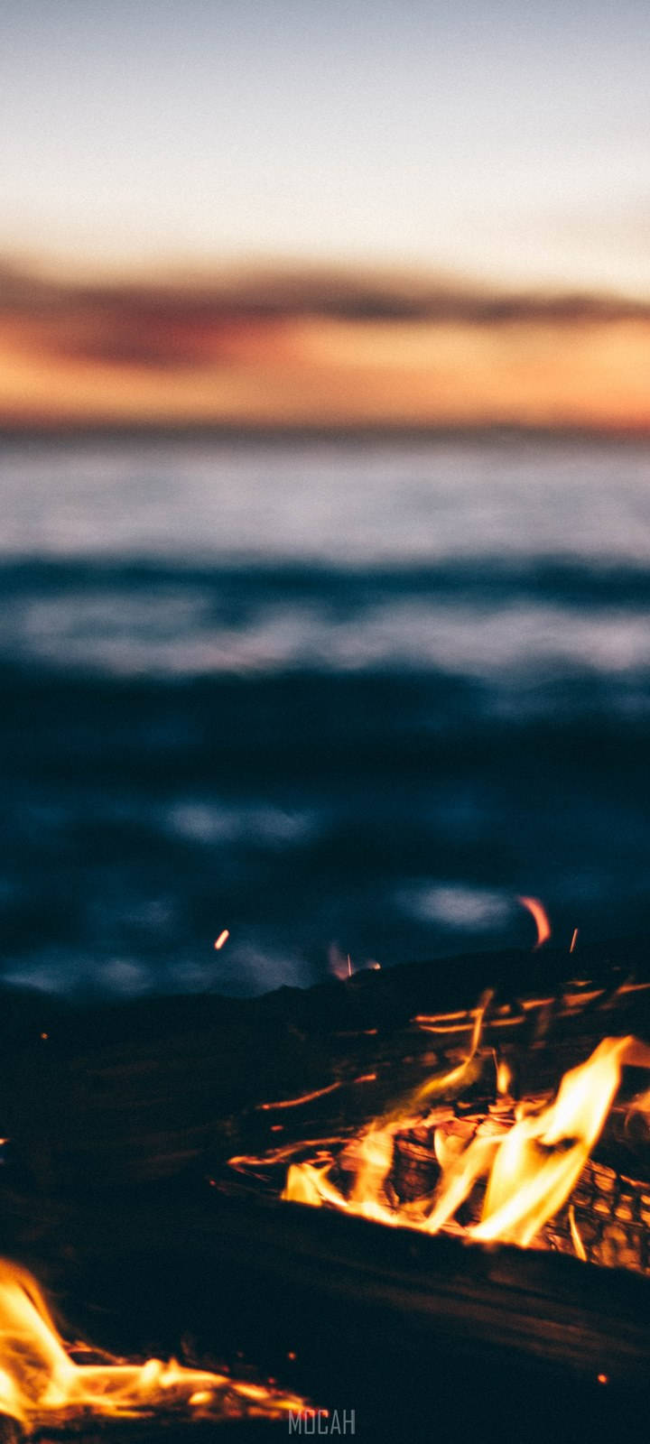 日落時分，營火在海灘上燃燒，背景是海浪。