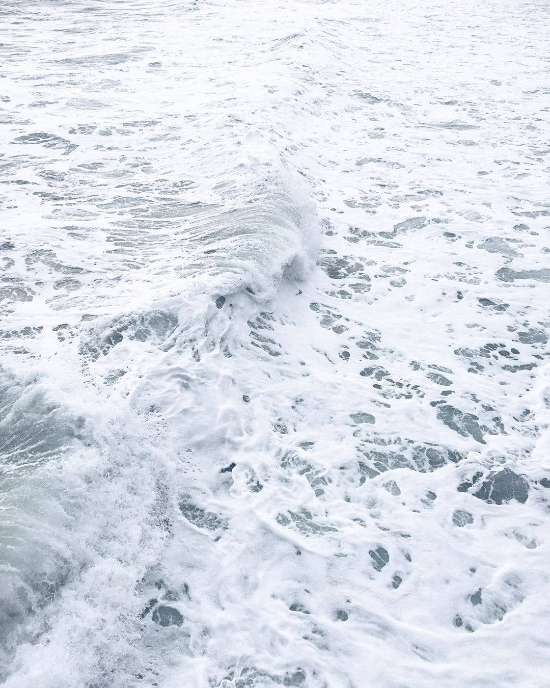 泡沫海浪翻滾而來，帶有紋理的白泡沫和灰藍色的海水。