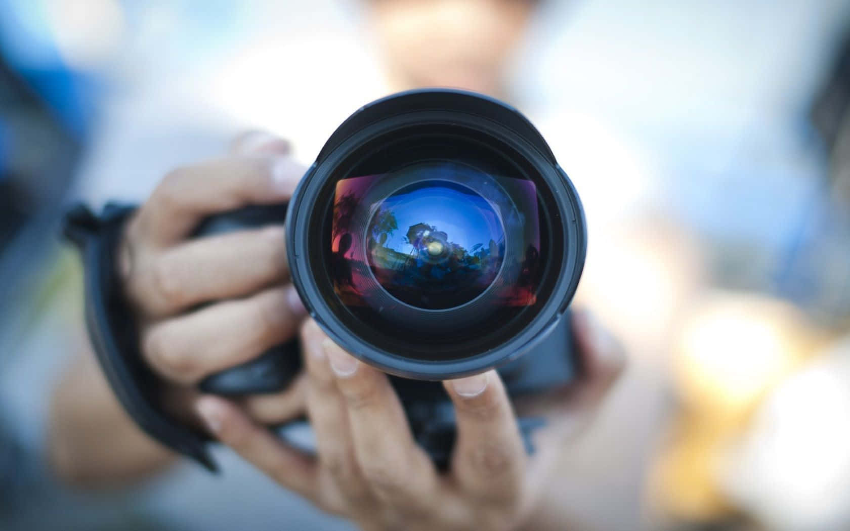Cameraman 桌布 壁紙 — 雙手拿著相機鏡頭的近距離特寫，鏡頭玻璃中反射出色彩繽紛的場景。