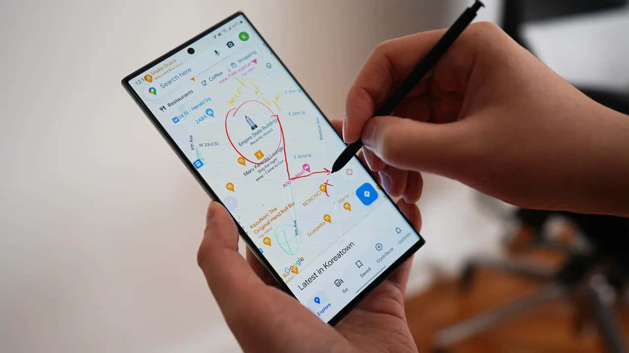 Samsung S23 Ultra 桌布 壁紙 — 特寫雙手使用觸控筆在智能手機上繪畫，手機顯示詳細的韓國城地圖，並有餐廳和咖啡店標記。