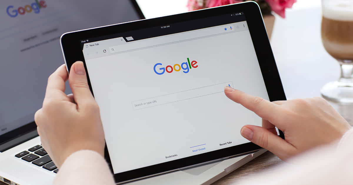 有人在附近有手提電腦和咖啡的情況下使用平板電腦搜尋Google。