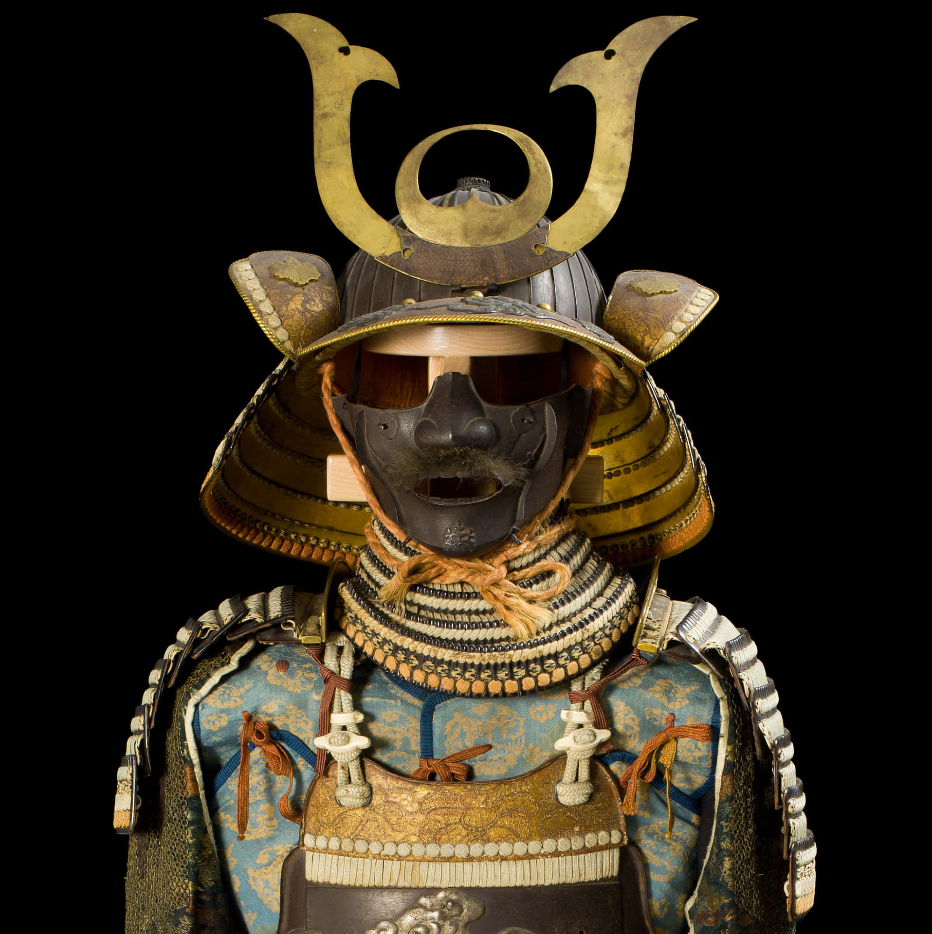  壁紙 — 一個詳細的特寫，展示了一件華麗的武士盔甲，帶有金色點綴和一個威嚇的面具，背景為黑色。