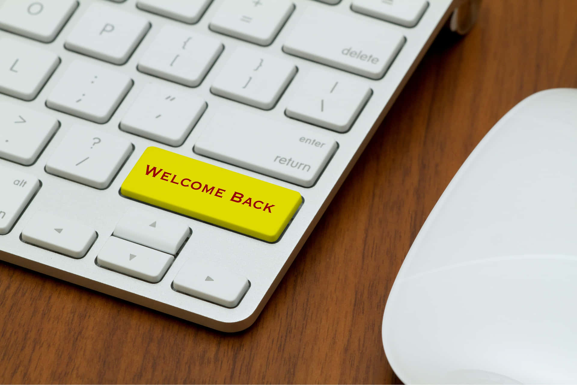  壁紙 — 銀色鍵盤的特寫，木桌上有一個亮黃色的「WELCOME BACK」鍵，旁邊有一個白色滑鼠。