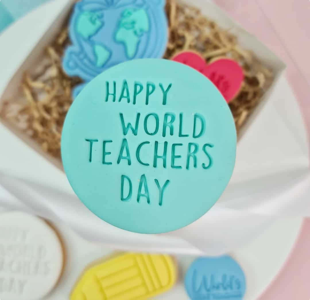  壁紙 — 一個青綠色圓形曲奇的特寫，上面有浮雕文字「HAPPY WORLD TEACHERS DAY」，周圍環繞著其他主題曲奇和一個禮物盒。