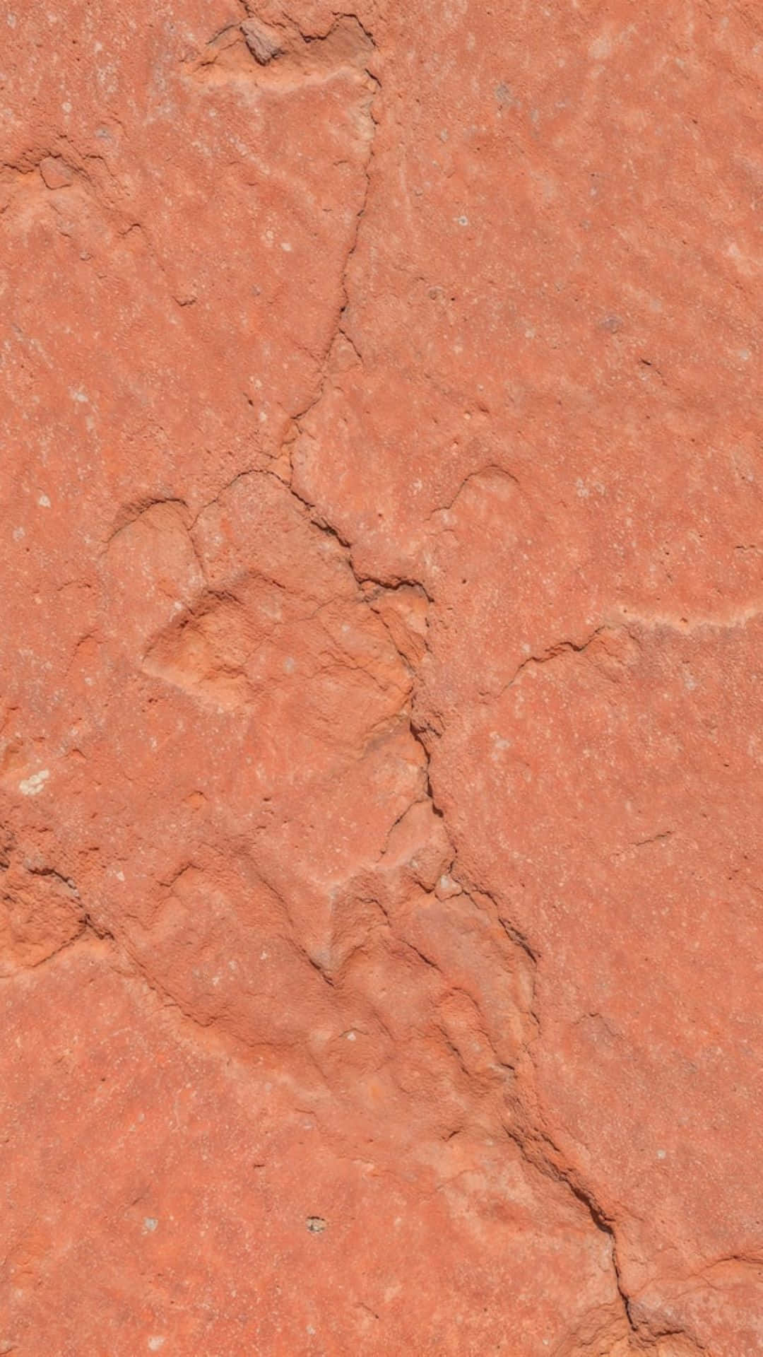  壁紙 — 帶有自然裂縫和粗糙紋理的橙紅色岩石表面特寫。