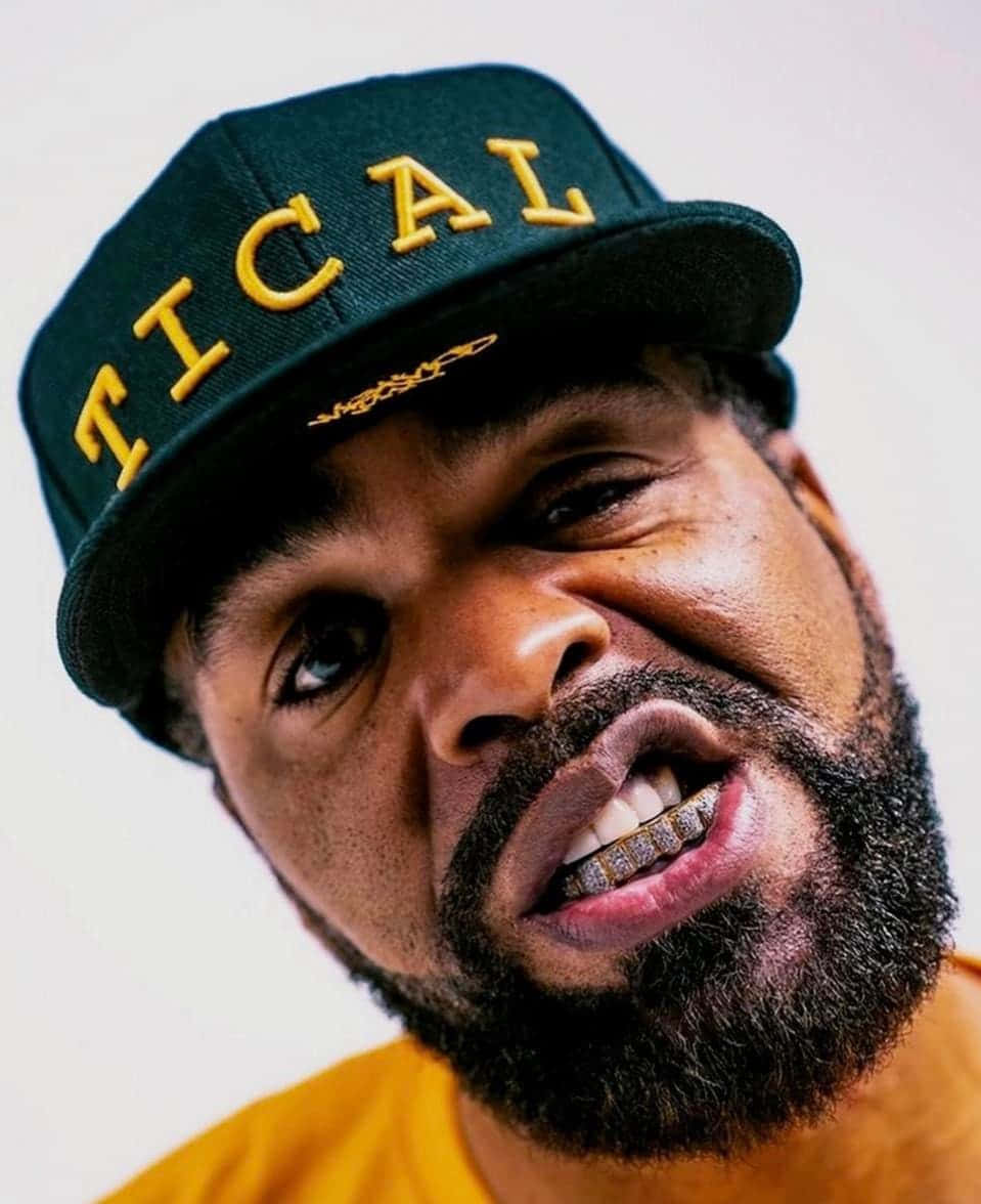  壁紙 — 一個留鬍鬚男人的特寫肖像，戴著一頂帶有黃色「TICAL」字樣的綠色帽子，以及金色牙套。