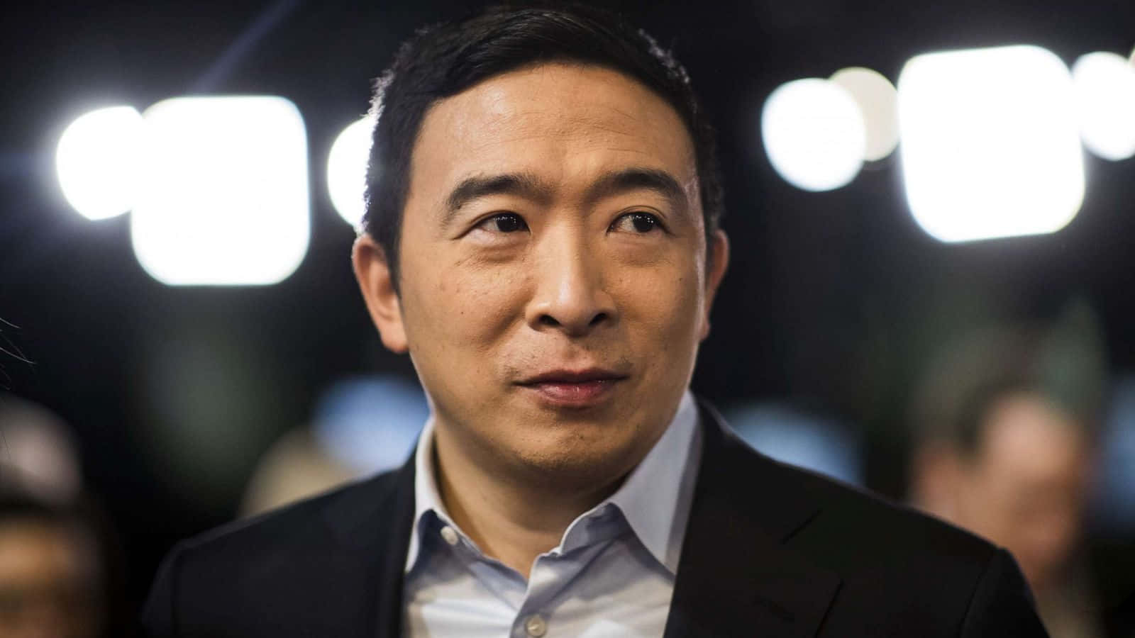 政治 桌布 壁紙 — 一個穿著西裝的男人向上望的特寫肖像，背後有明亮的燈光模糊。