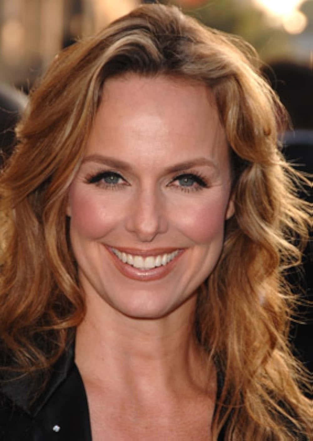 Melora Hardin 桌布 壁紙 — 一位微笑女性的特寫肖像，擁有波浪金髮和明亮的藍色眼睛，穿著黑色上衣。