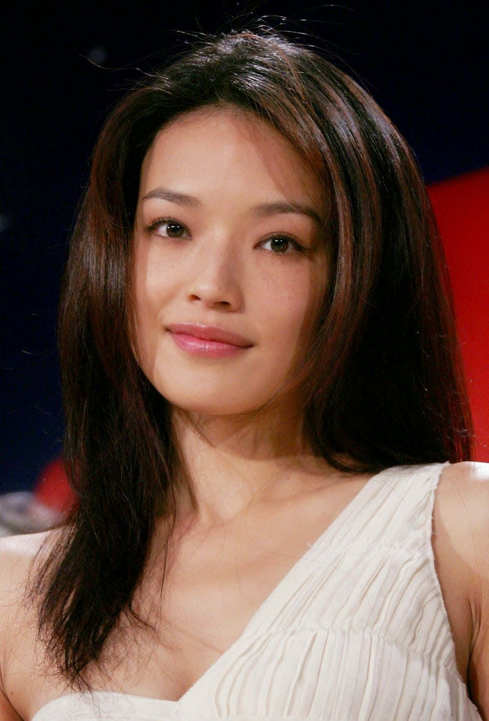 Shu Qi 桌布 壁紙 — 一位深色頭髮、帶著溫柔微笑、身穿白色連衣裙的女性在深色背景前的特寫肖像。
