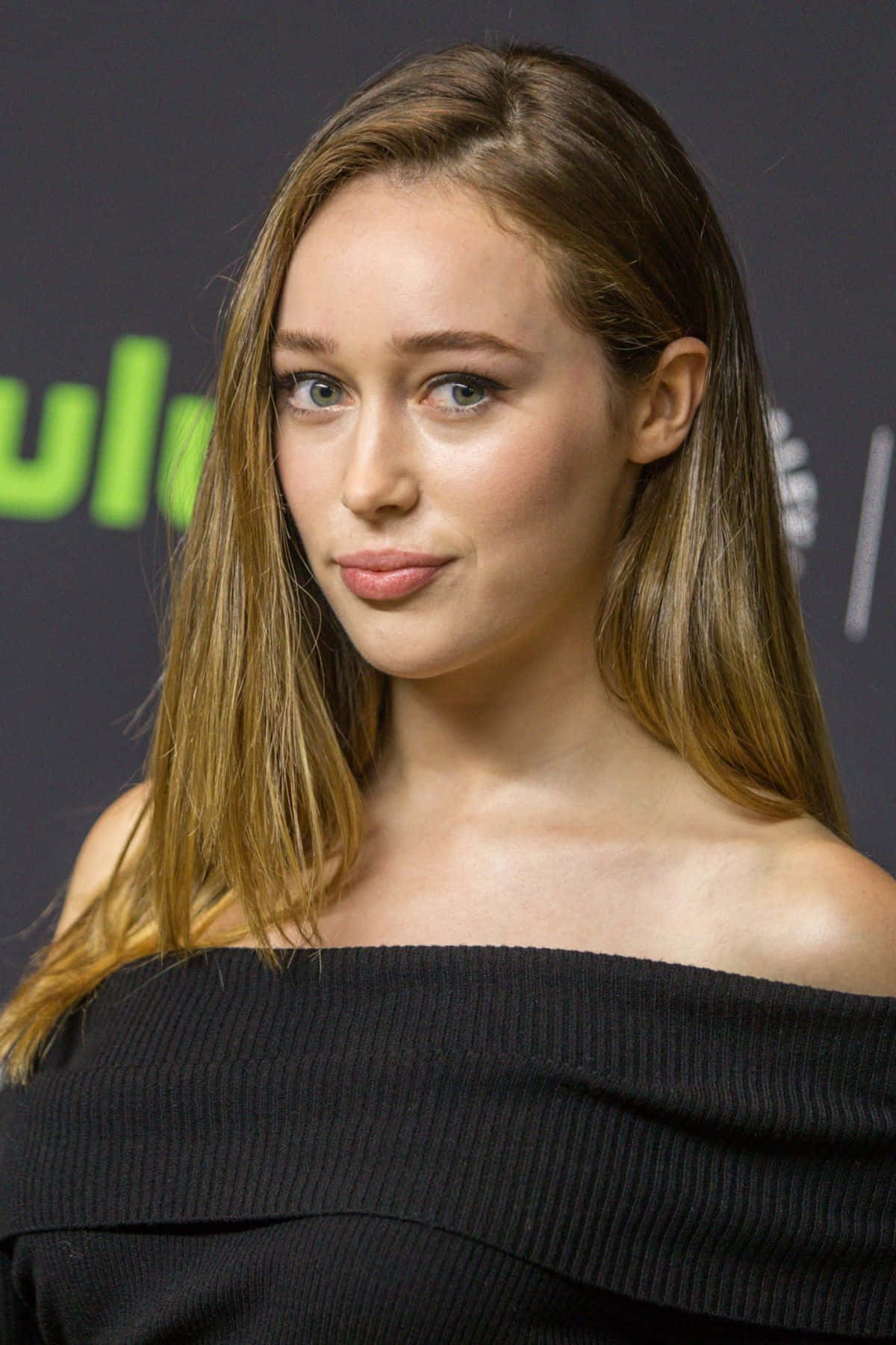 alycia debnam carey 桌布 壁紙 — 一位長髮棕髮女性穿著黑色露肩上衣，在帶有綠色標誌元素的深色背景下的特寫肖像。