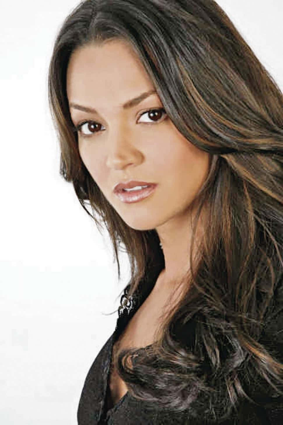 Paula Garcés 桌布 壁紙 — 一個特寫肖像，一位擁有長深棕色波浪髮和強烈棕色眼睛的女性，在純白色背景前直視鏡頭。