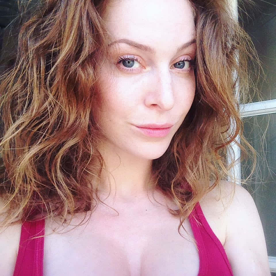 Esmé Bianco 桌布 壁紙 — 一位擁有波浪赤褐色頭髮和藍色眼睛的女性穿著粉紅色上衣的特寫肖像。