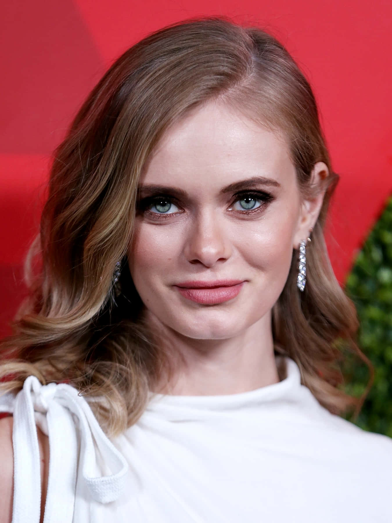 Sara Paxton 桌布 壁紙 — 一位擁有波浪金髮和藍眼睛的女性，穿著白色連衣裙和鑽石耳環，以紅色背景為襯的 close-up 肖像。