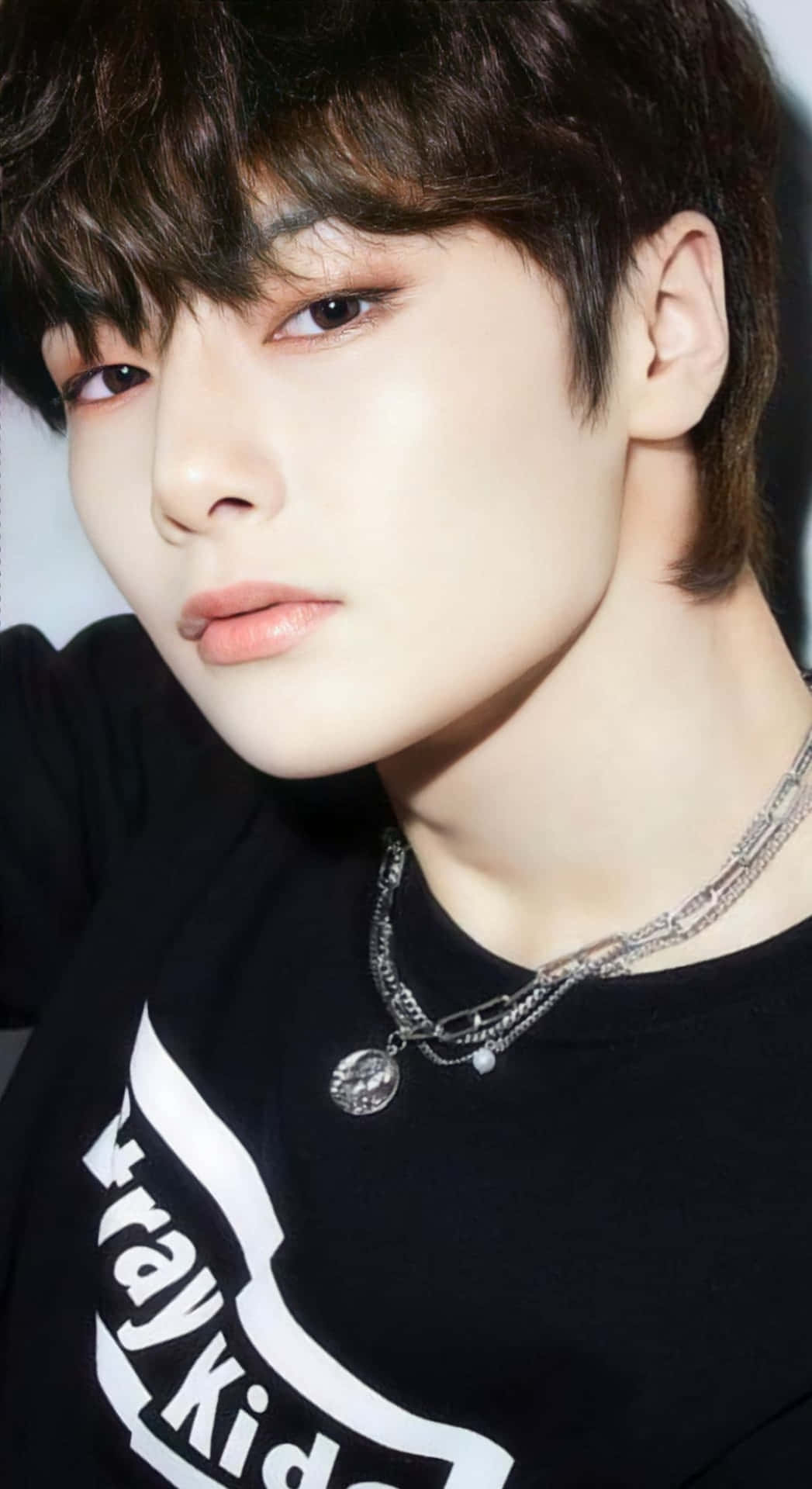  壁紙 — 年輕黑髮男子佩戴多層銀色項鍊，身穿黑色Stray Kids T恤的特寫肖像。